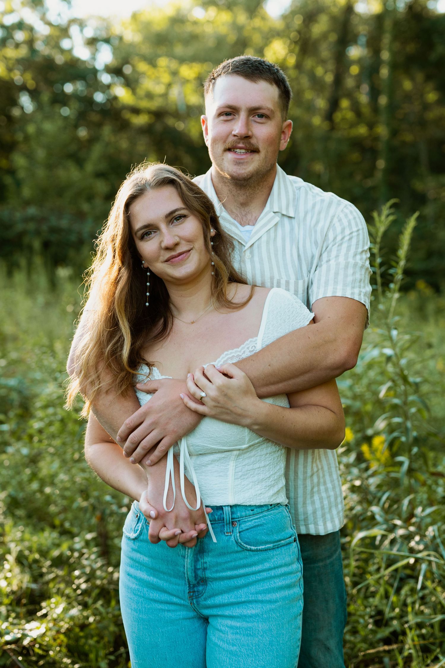 Couple in coordinated outfits sharing intimate moment in garden with summer foliage.