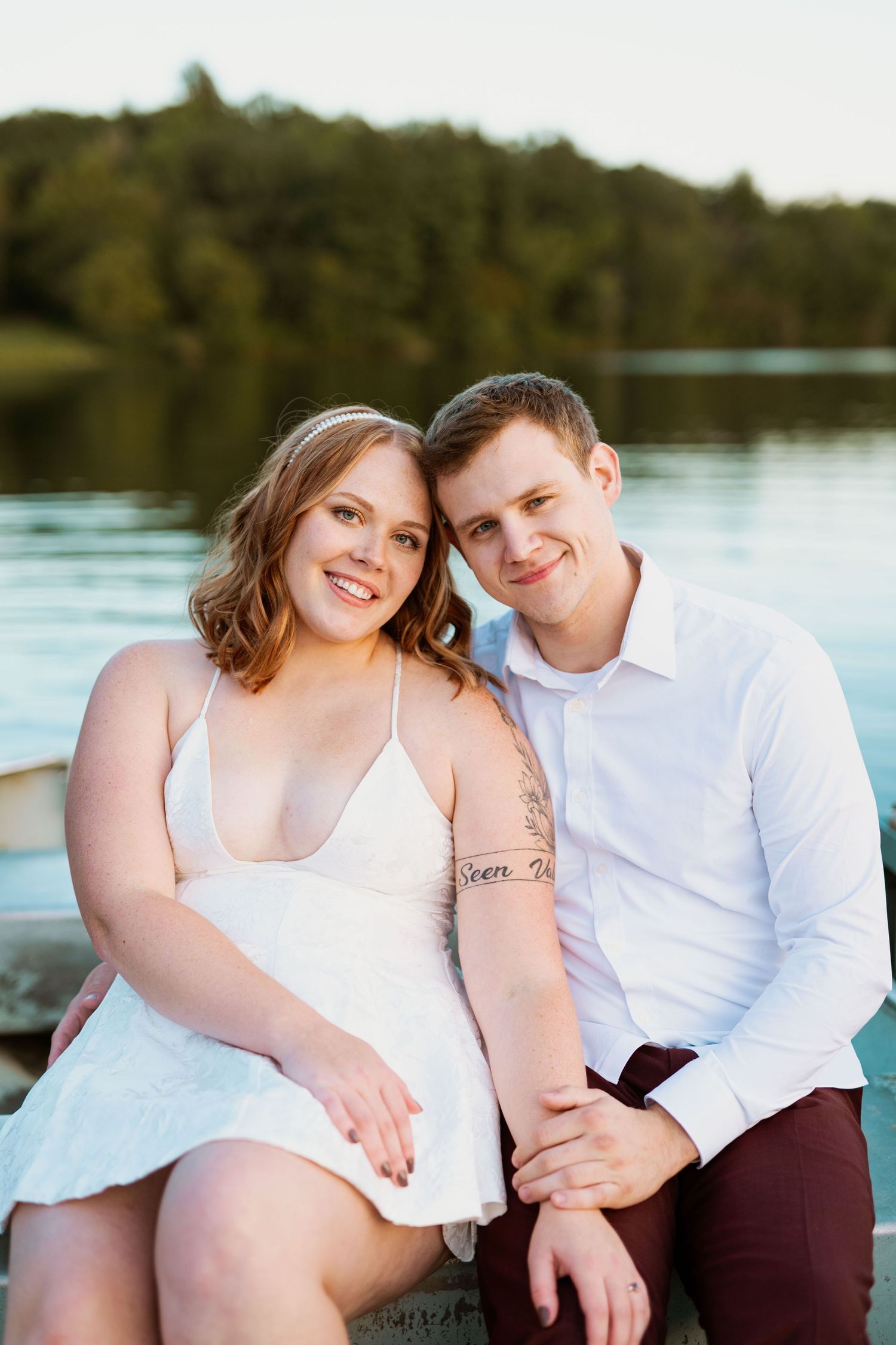 A couple poses together on a dock during a lakeside photo session at sunset.