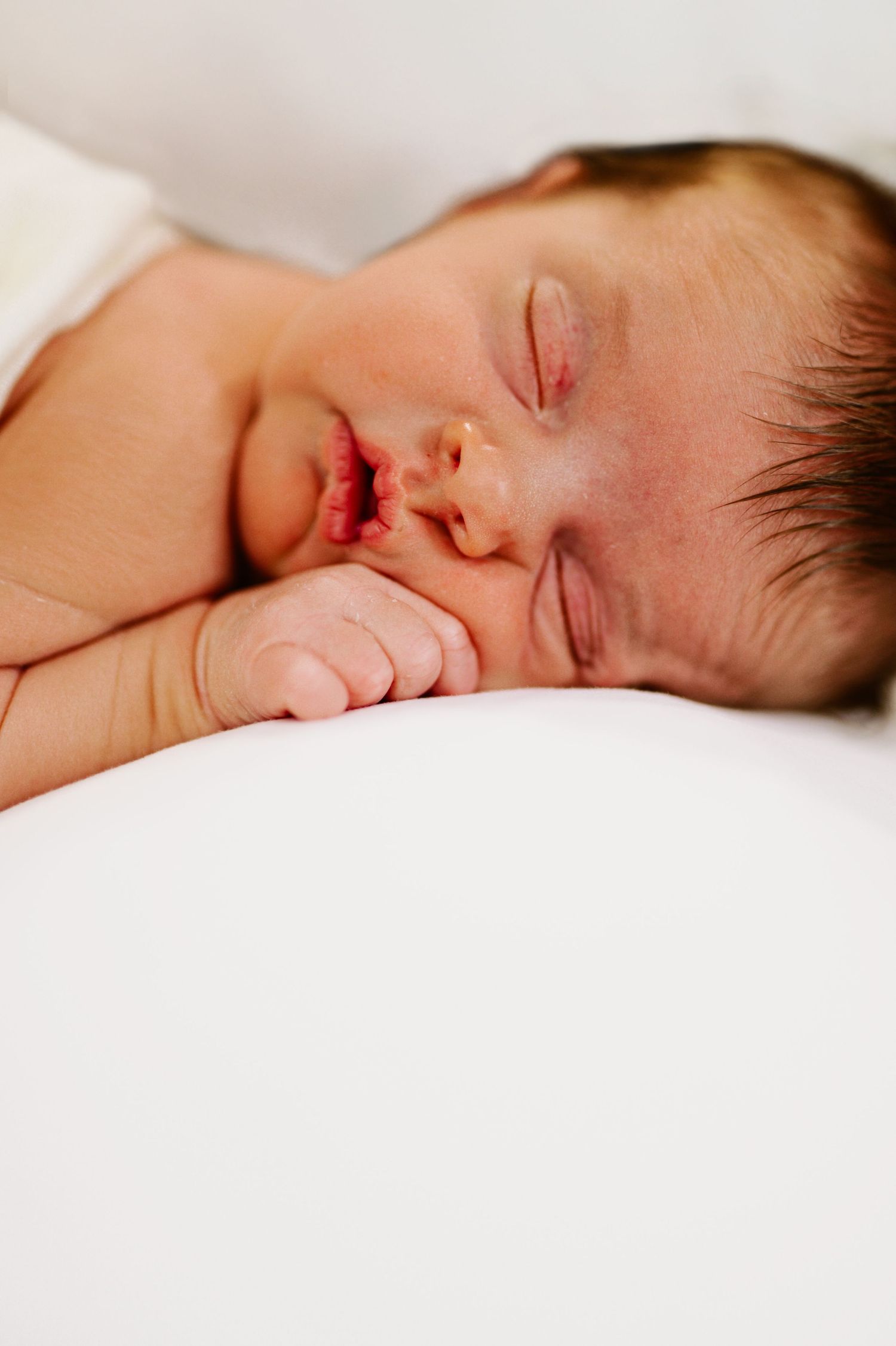 Closeup of sleeping newborn baby with tiny hand near face.