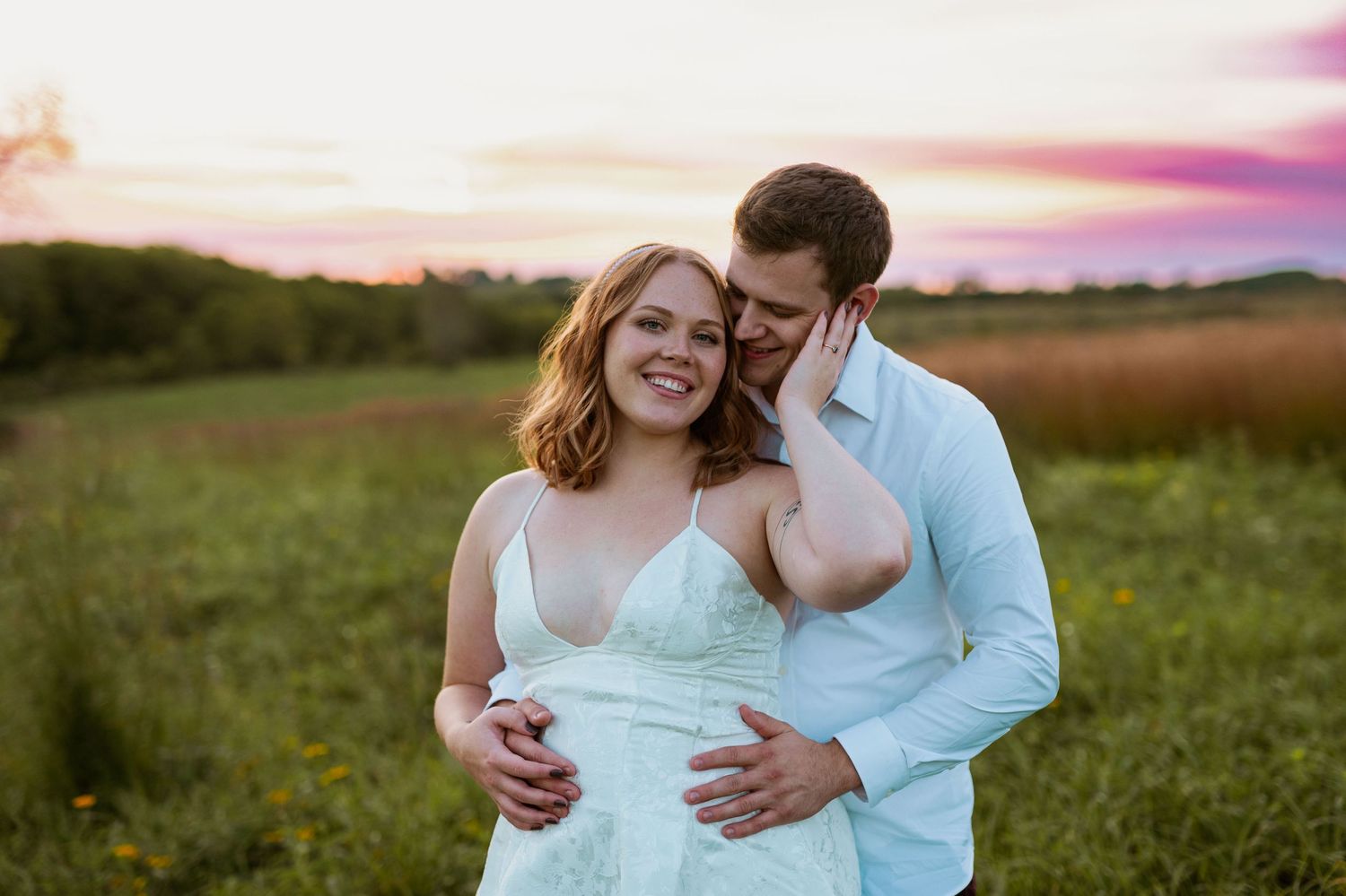 A couple shares a tender moment in a field during sunset.