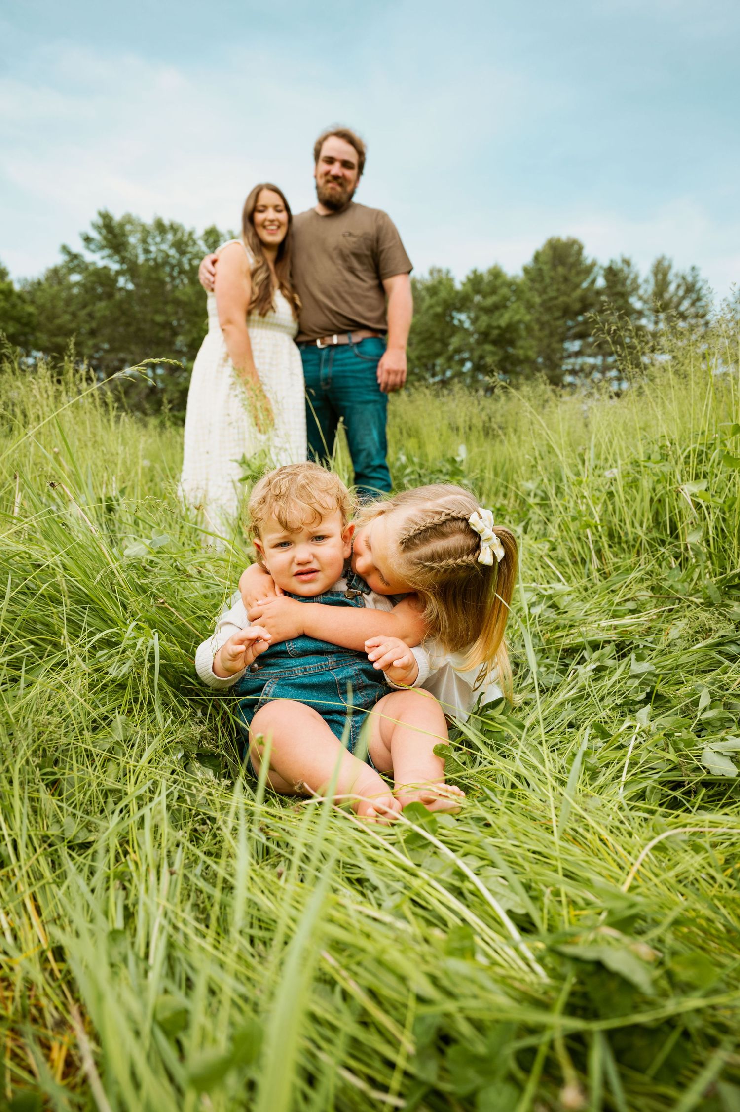 A family poses together in a grassy summer meadow with tall green grass and blue sky.