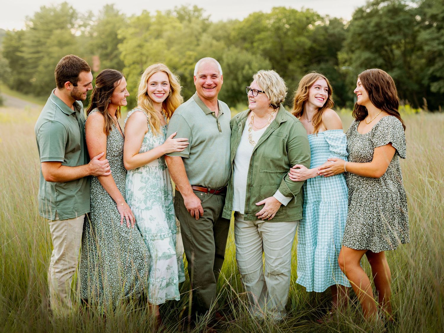 Family portrait session in a grassy field showing casual poses and coordinated outfits in blue and green tones.