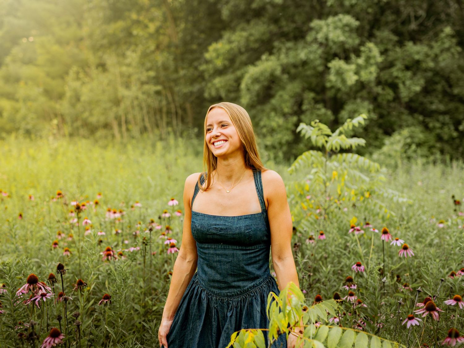 A woman in a dark green dress poses joyfully in a wildflower meadow during golden hour.