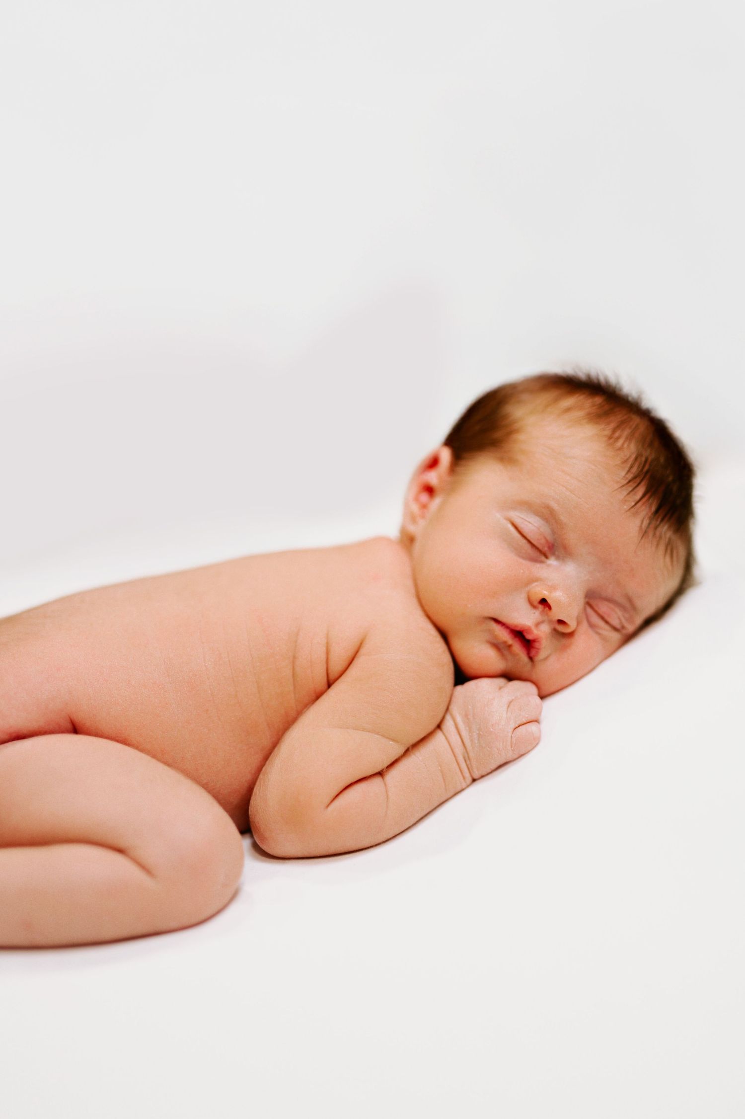 Sleeping baby in natural pose against white backdrop.