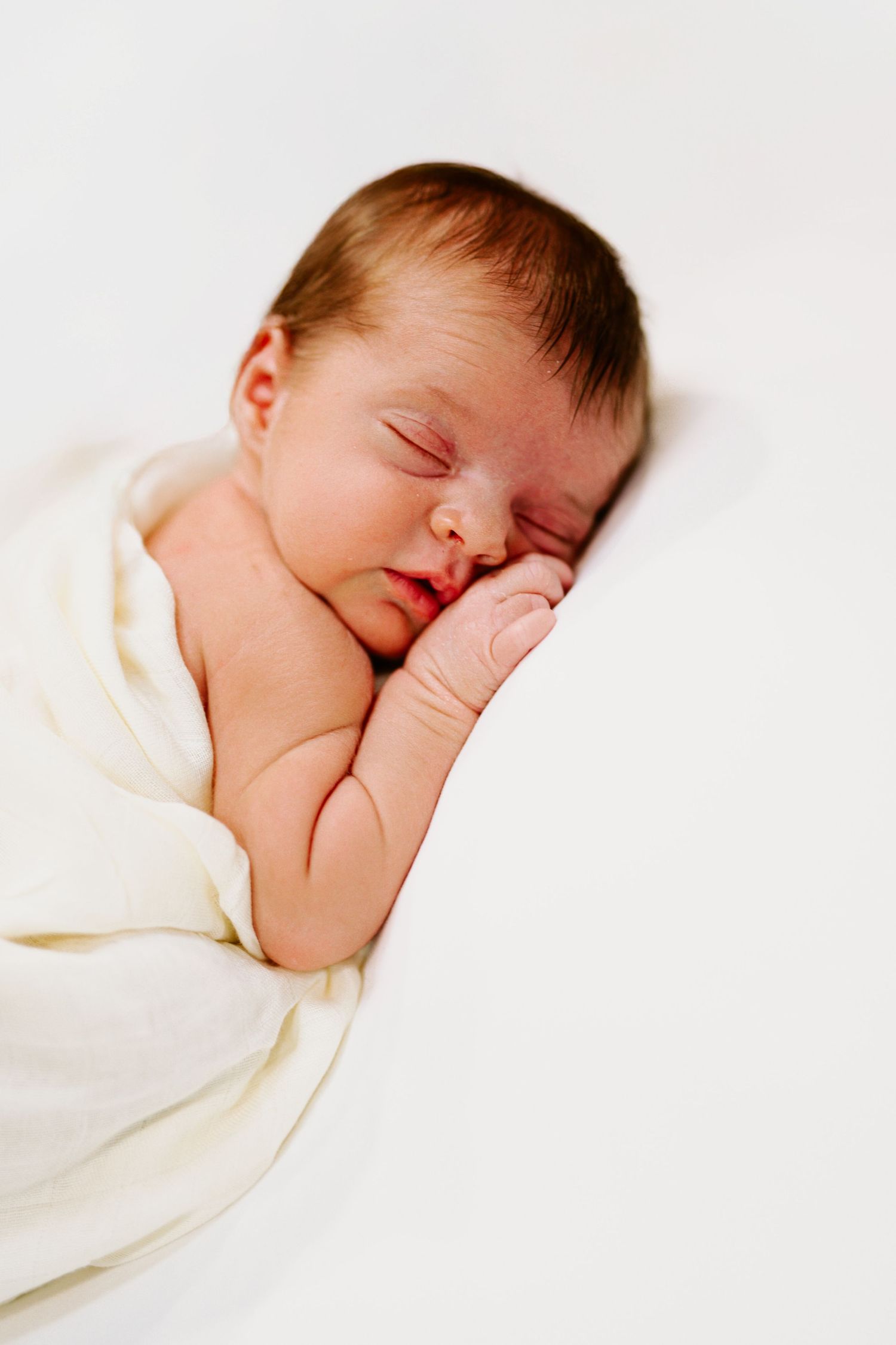 A peaceful sleeping newborn wrapped in soft cream colored blanket.