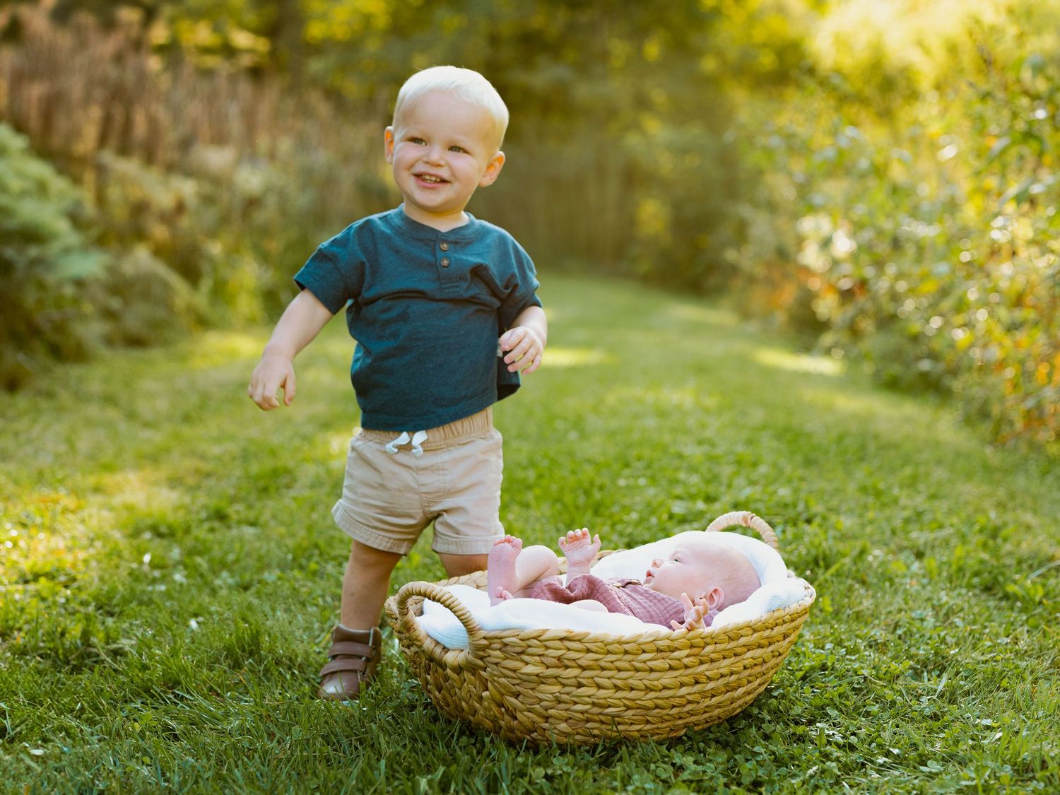 A small child in a navy shirt plays outdoors near a woven basket on green grass in golden sunlight.