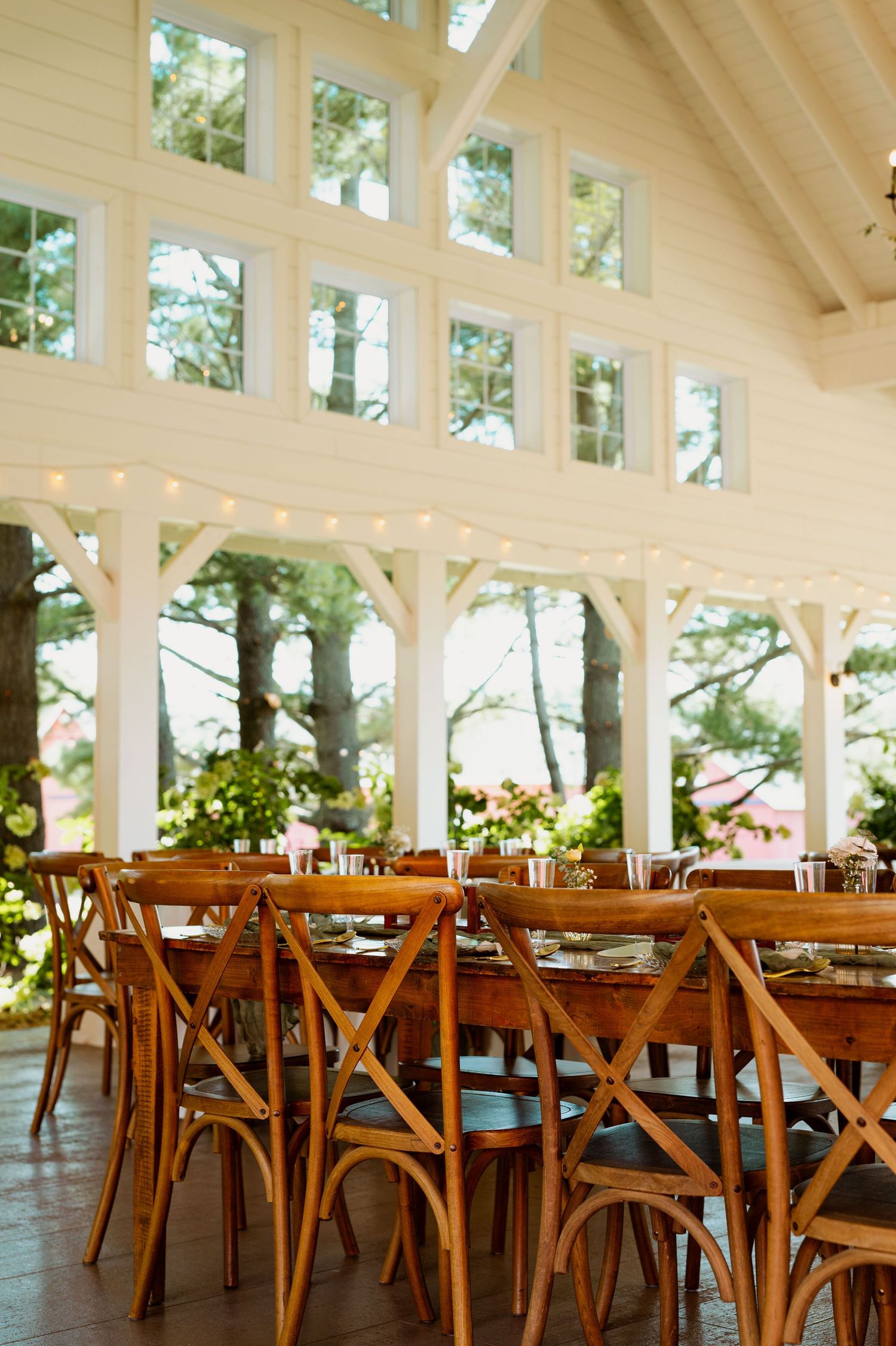 Rustic wooden cross-back chairs and tables arranged in a bright white pavilion with natural lighting.