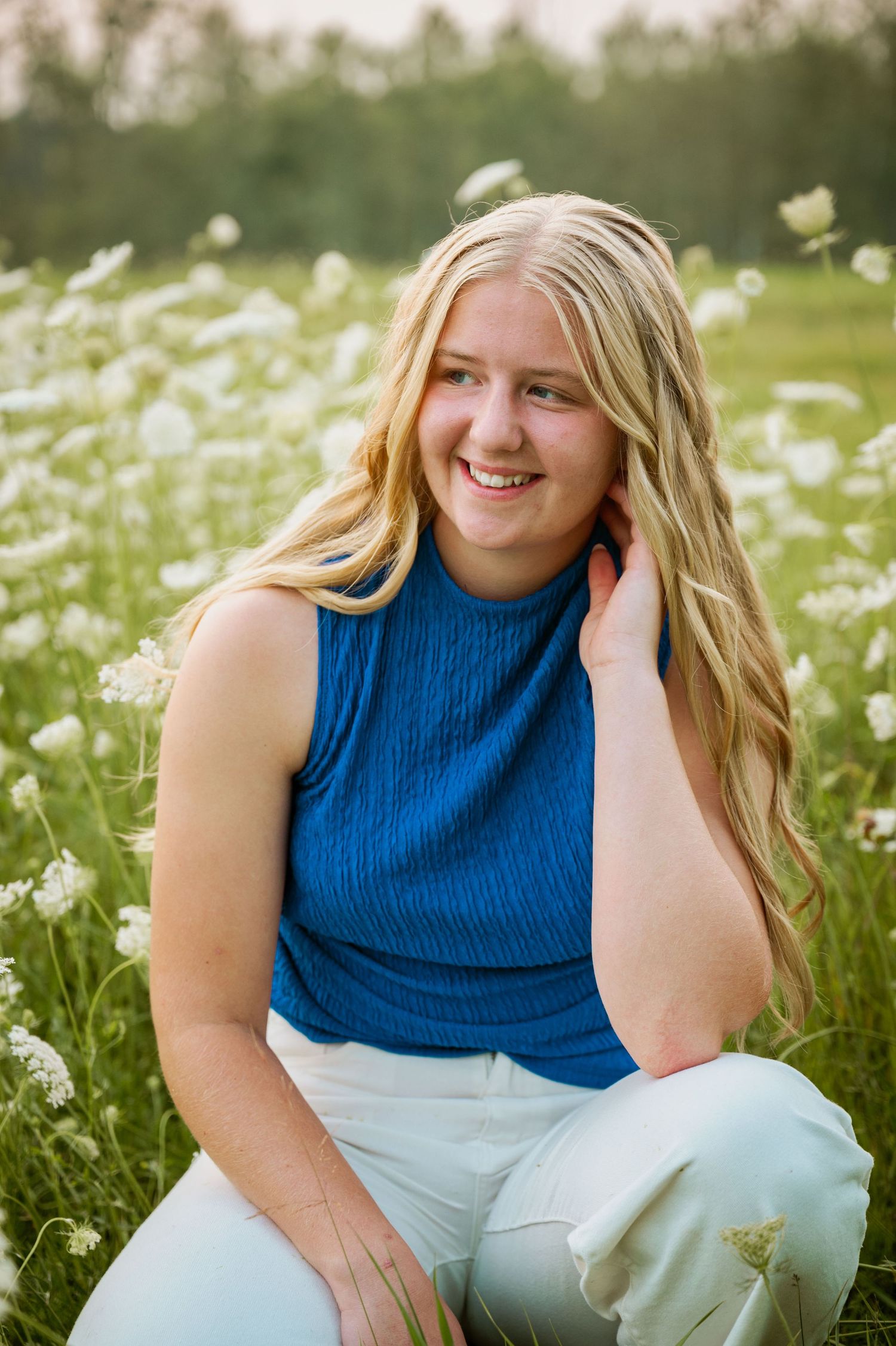 Portrait session in a meadow of white wildflowers wearing a blue sleeveless top.