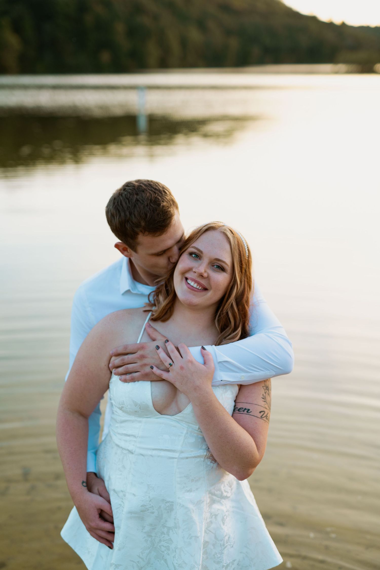 A couple shares a tender moment by a lake during golden hour.