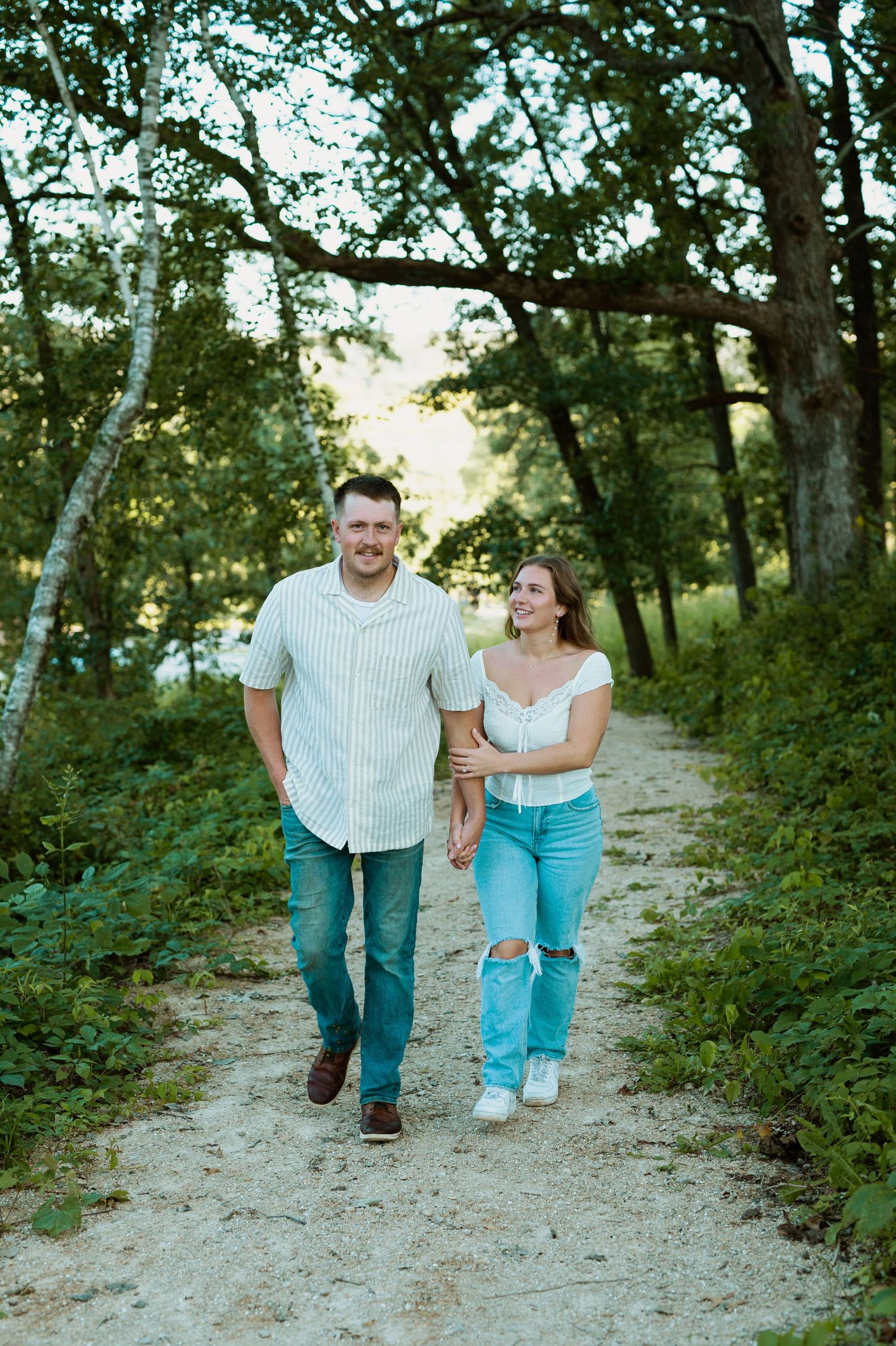 Couple walking together on nature trail through wooded area in summer.