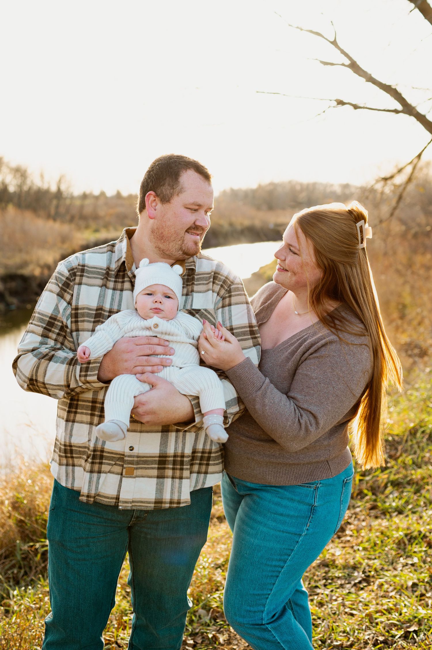 A family shares a tender moment outdoors during golden hour, with a small baby bundled in warm clothes.
