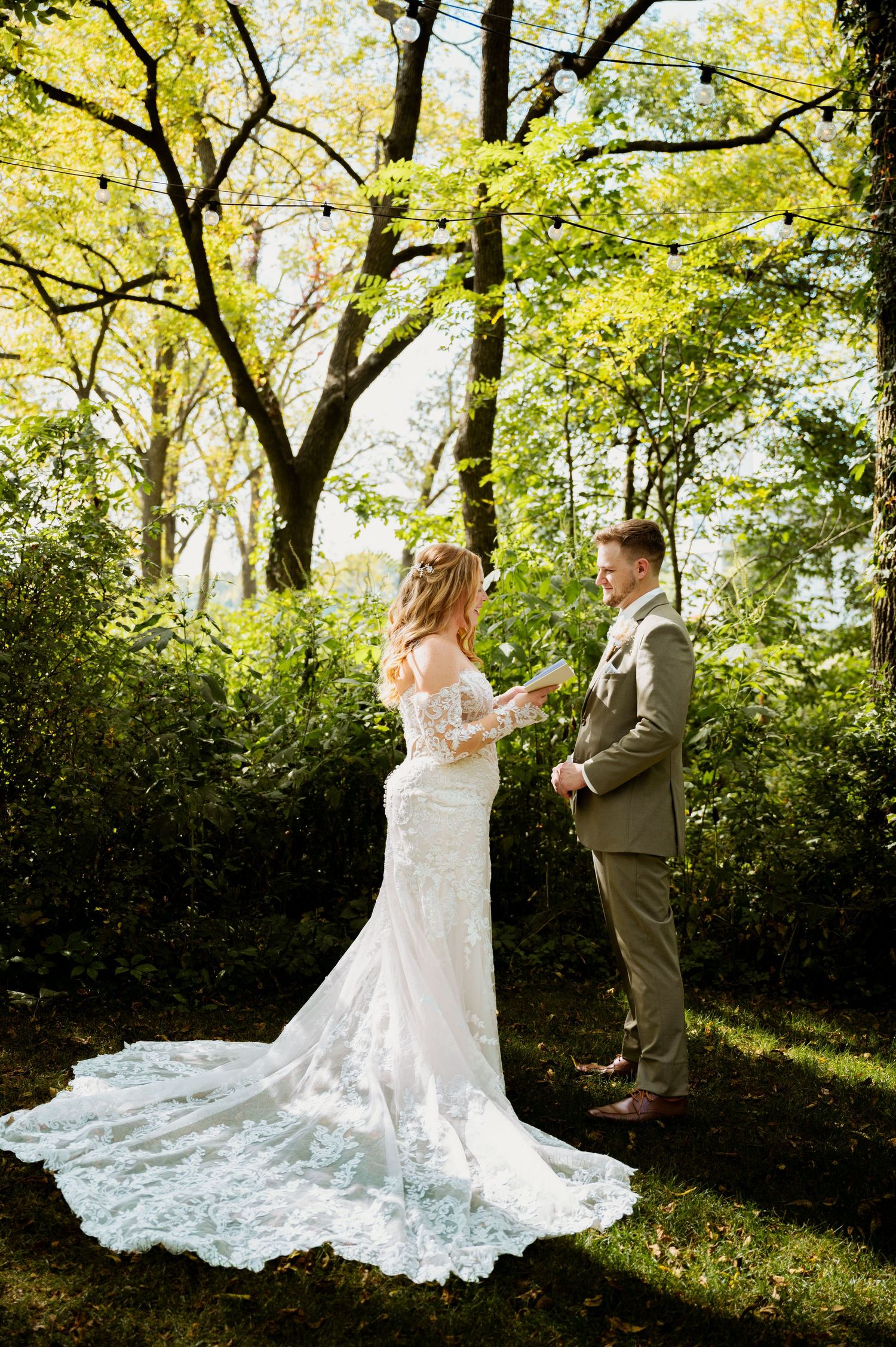 Romantic wedding couple dancing together in a sunlit garden setting with flowing white lace dress.