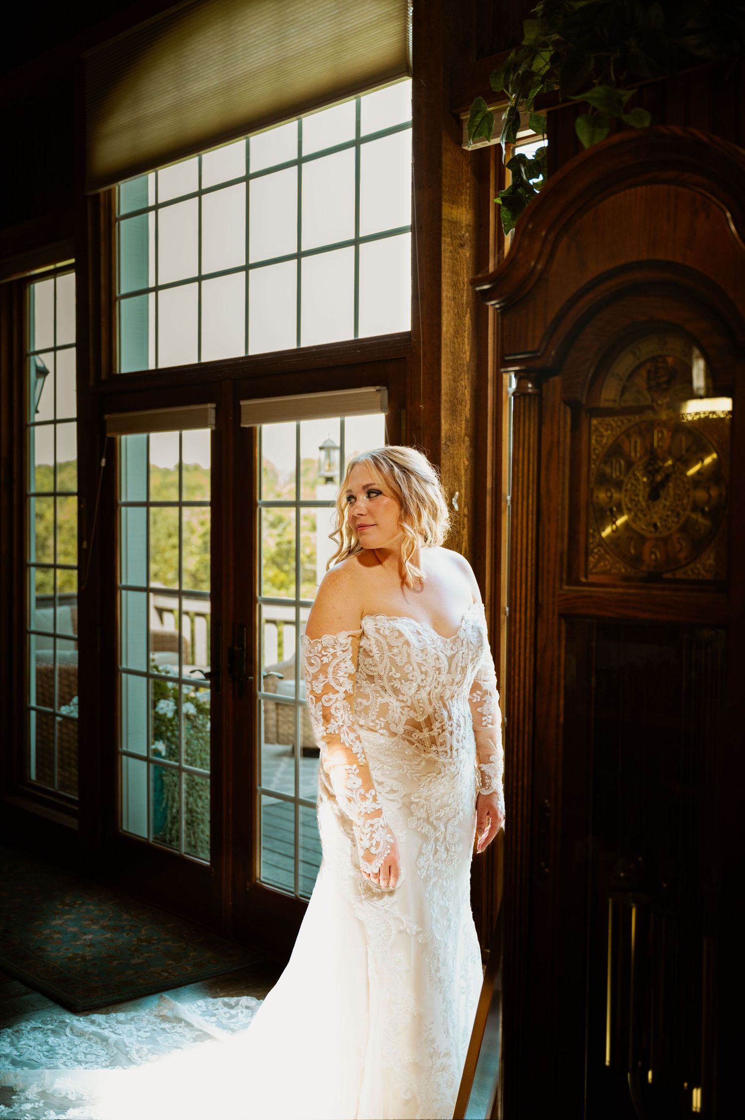 Elegant wedding dress with lace details shown in window-lit interior space.