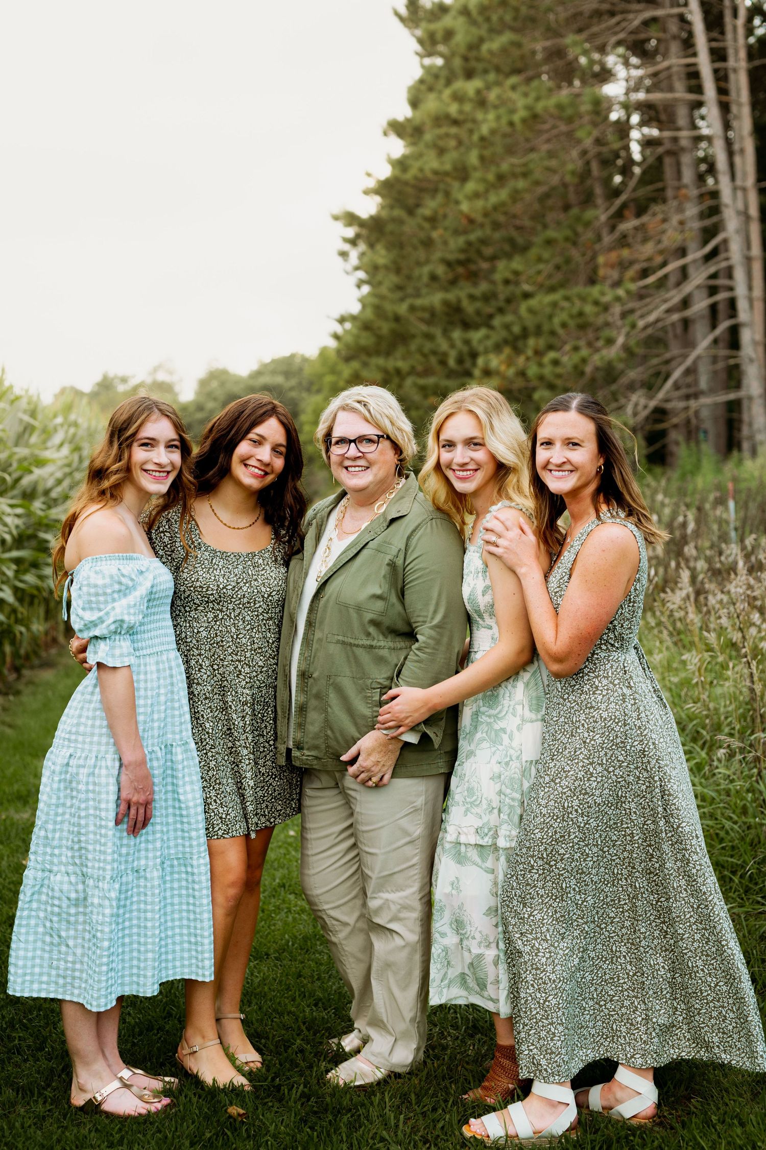 A group of friends pose together outdoors in coordinated casual outfits among trees and greenery.