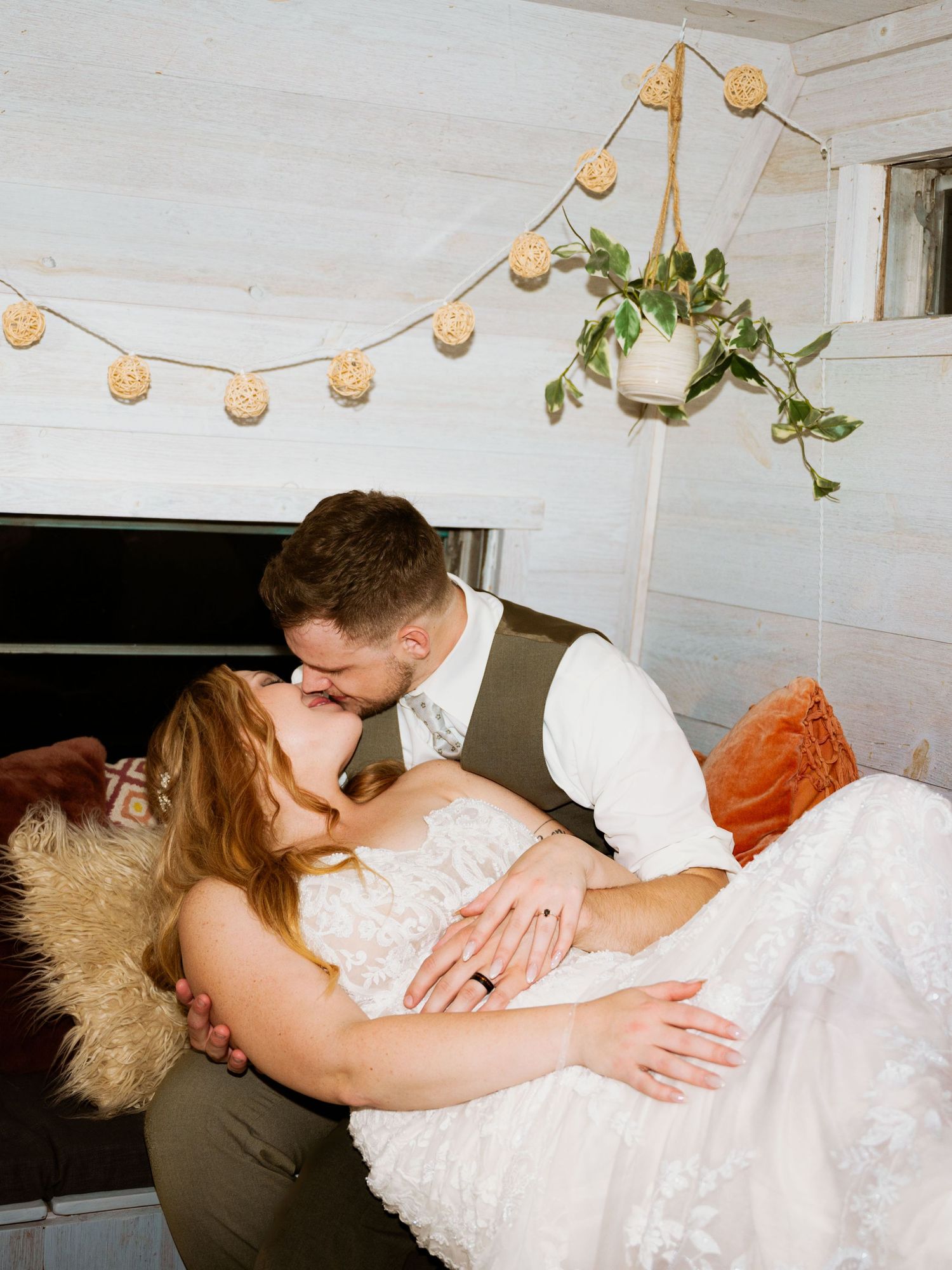 A romantic couple shares tender moments on a couch under warm string lights at their wedding reception.