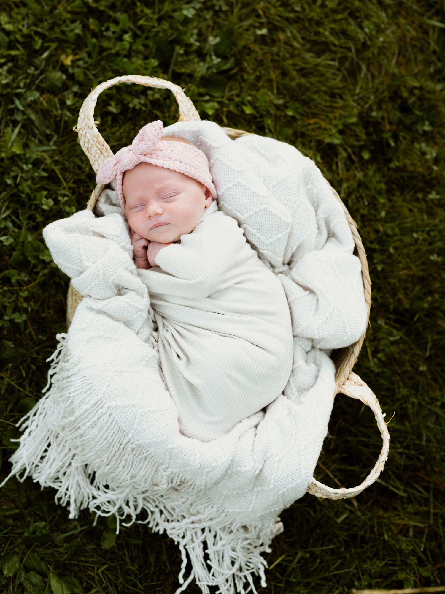 Newborn baby wrapped in soft white blanket resting on green grass background.