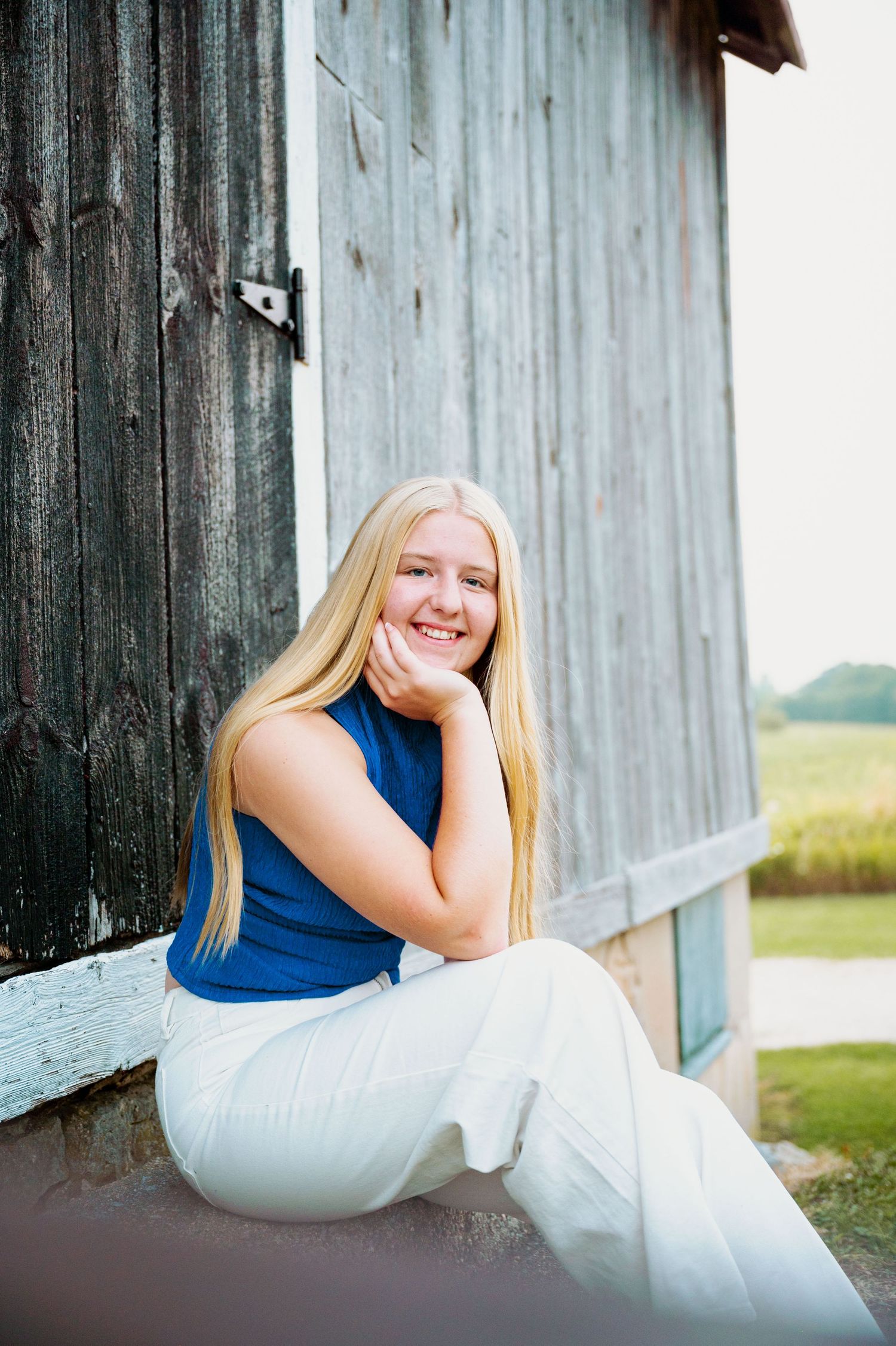 A series of casual outdoor portraits shows someone in a navy top and white pants sitting and reclining against a rustic barn wall.