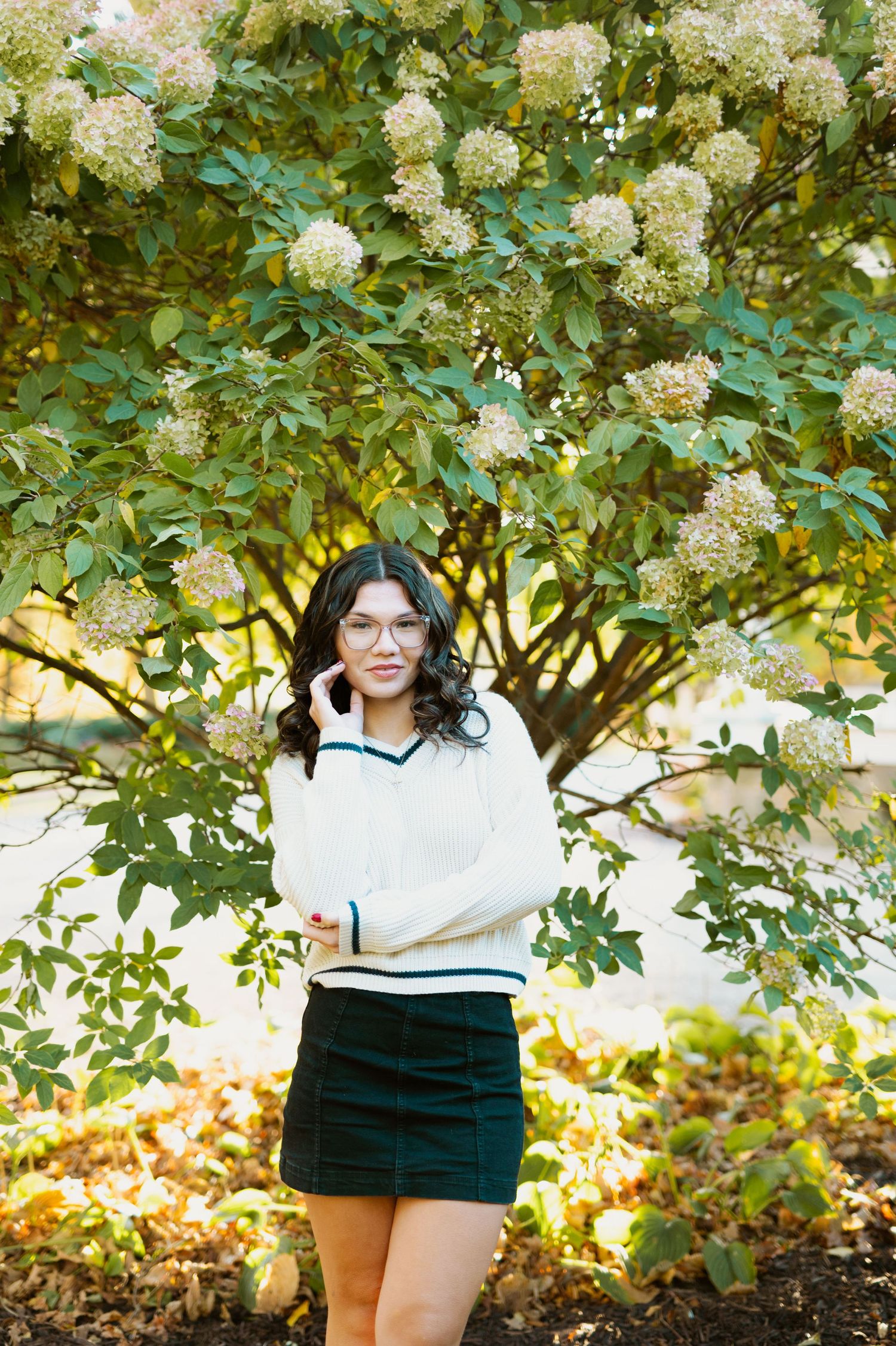 An outdoor photo shoot in autumn with flowering bushes and natural sunlight creating a warm ambiance.