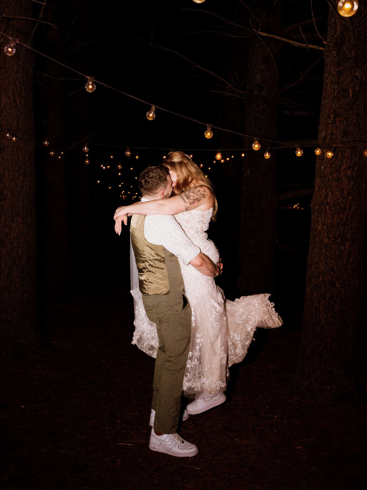A nighttime wedding celebration under twinkling string lights in a wooded setting.