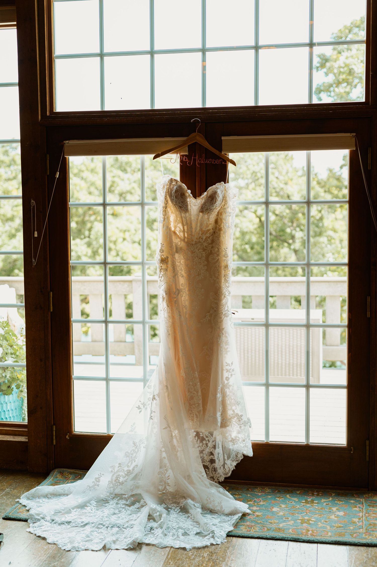 Beautiful lace wedding dress hanging in front of large windows with natural light streaming through.