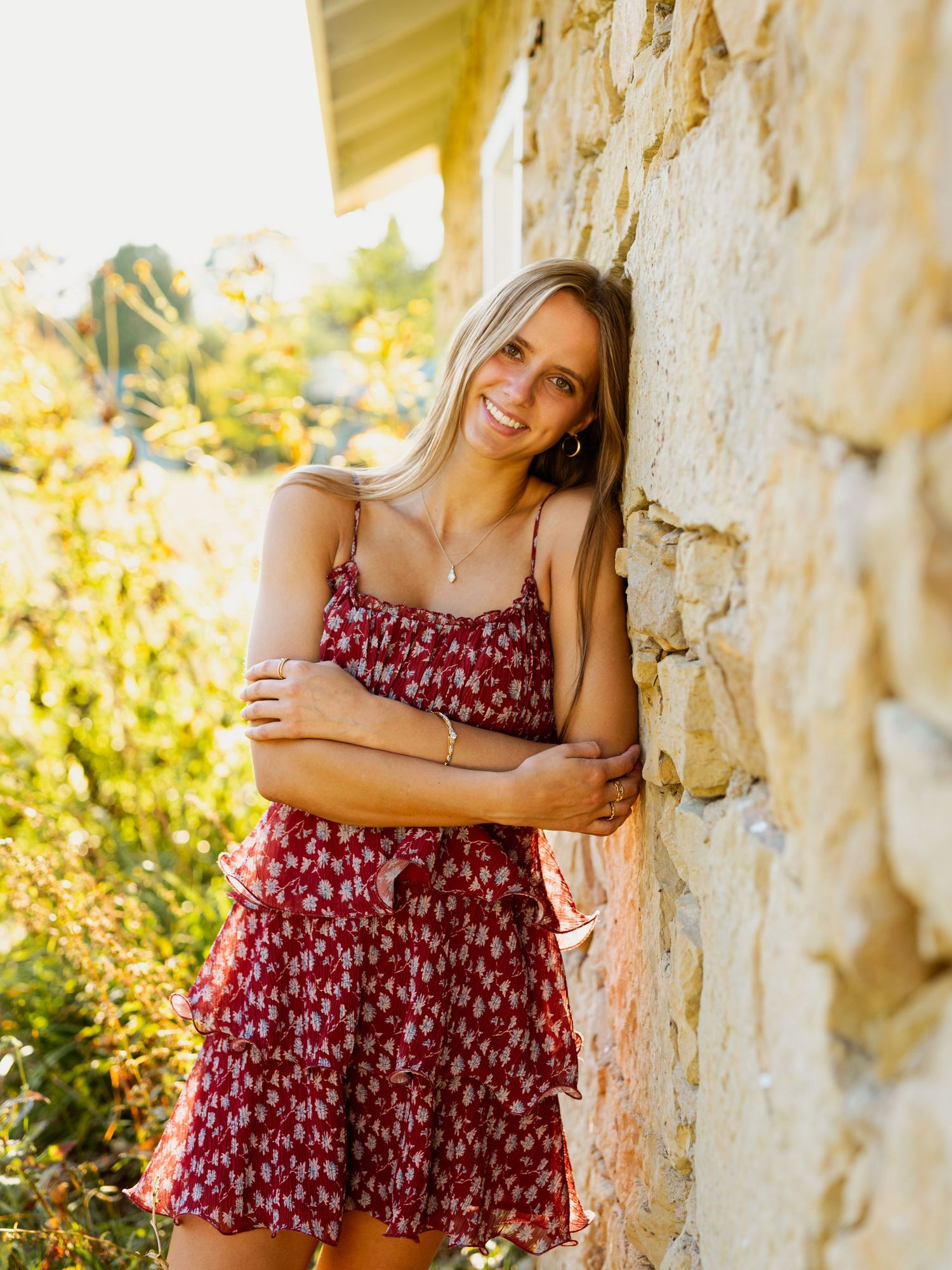Summer portrait series against rustic stone wall with floral burgundy dress in warm golden sunlight.