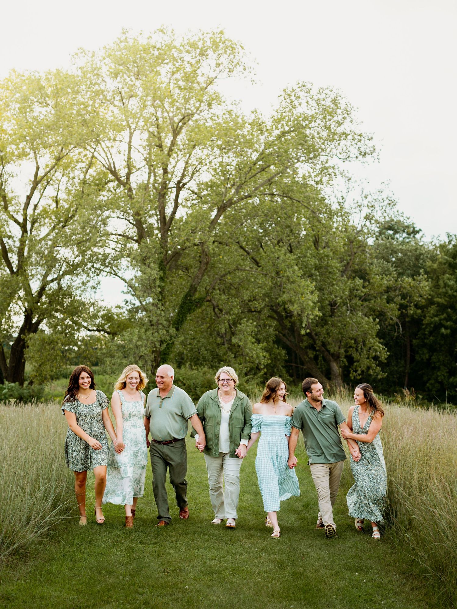 A group walks together through a grassy field with tall trees in the background on a summer day.
