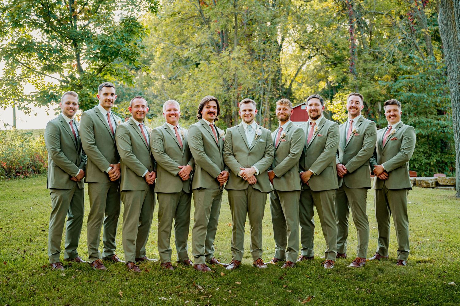Groomsmen in matching gray suits pose together on a grassy lawn.