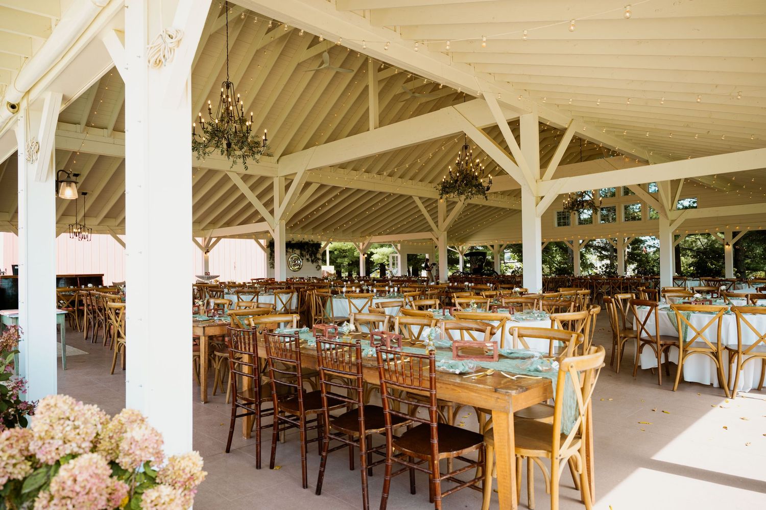 Large white tent venue set up with wooden cross-back chairs and tables for an elegant outdoor wedding.