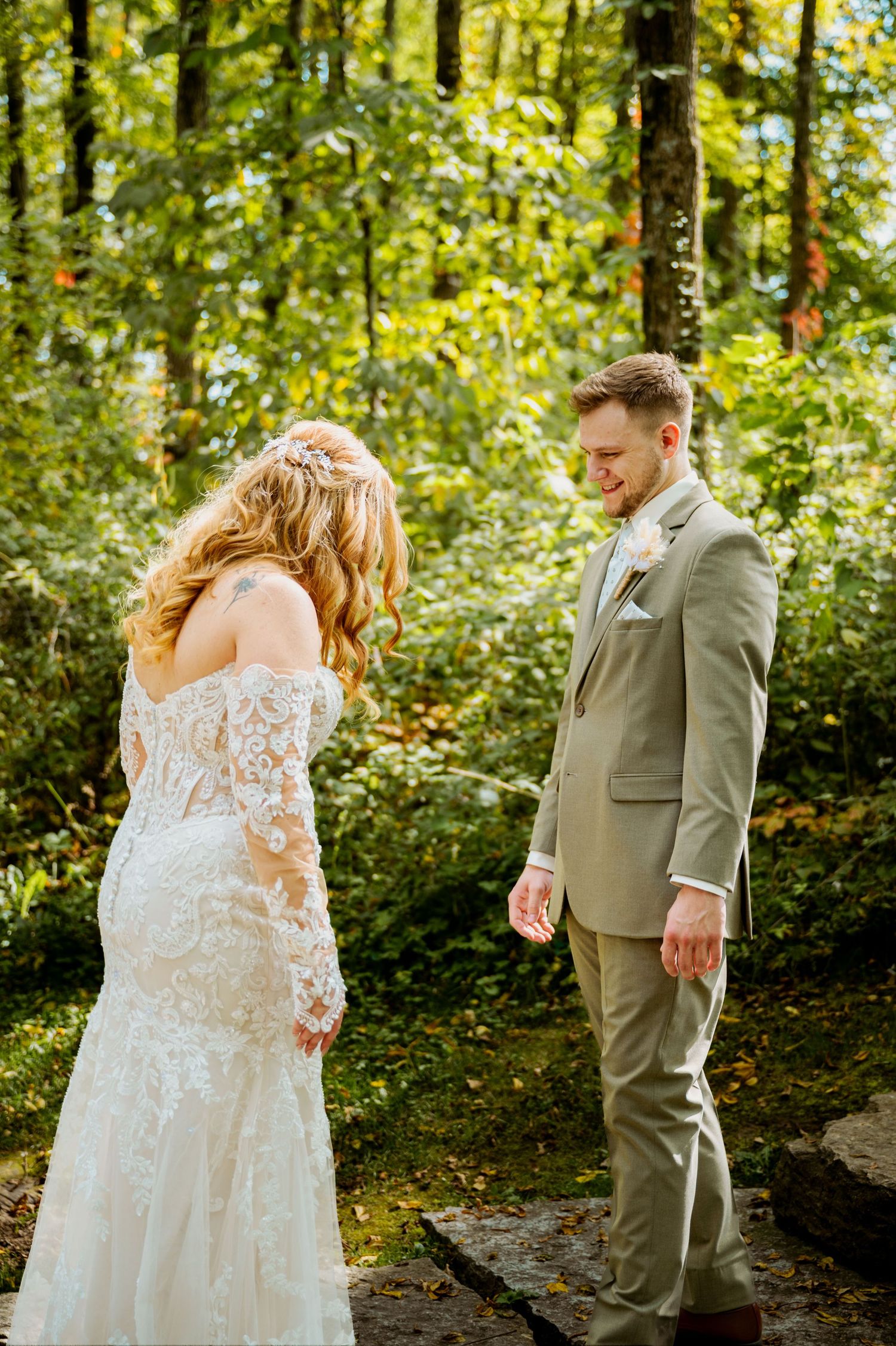 A wedding couple shares an intimate first look moment in a sunlit forest setting.