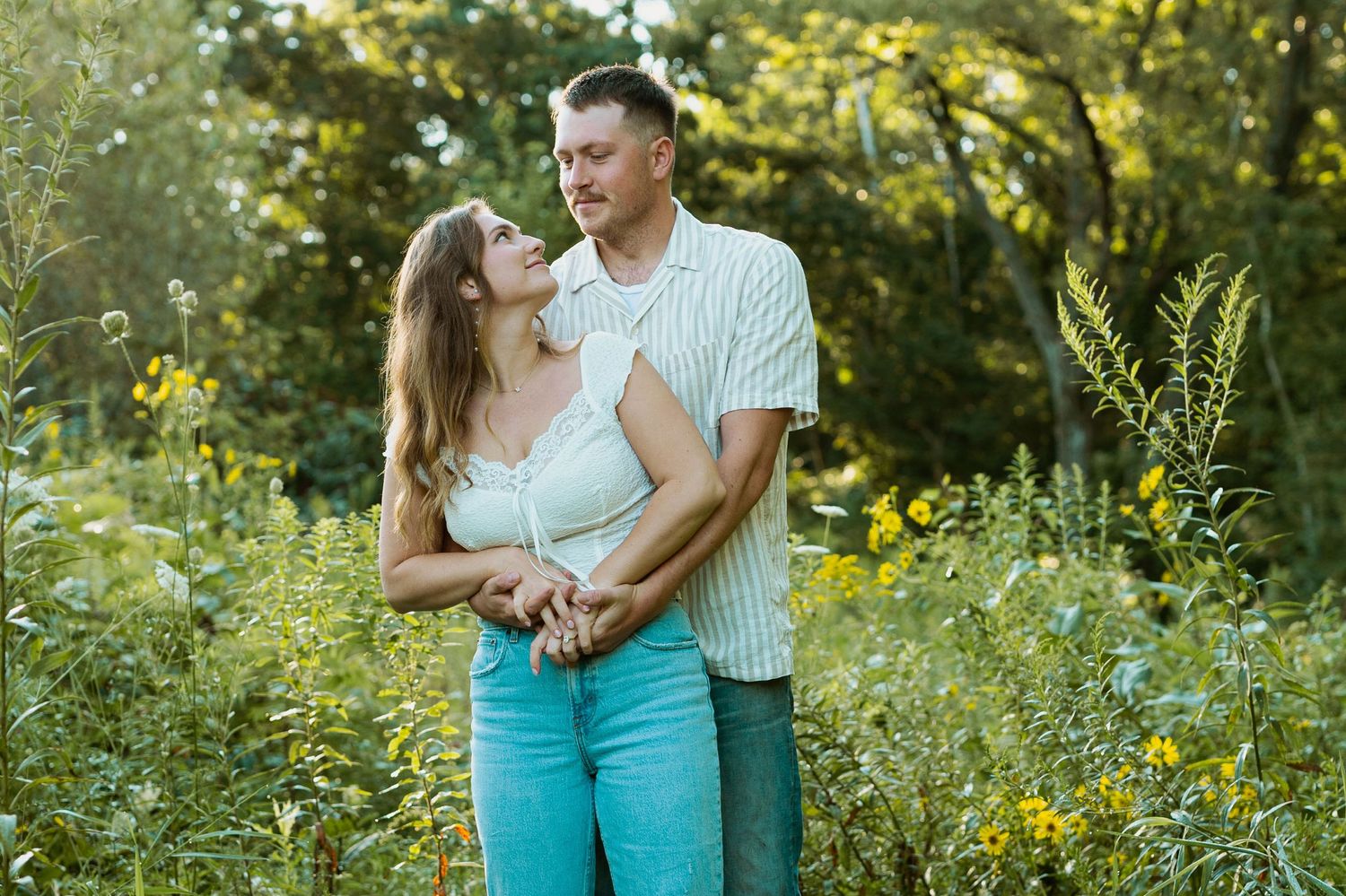 Romantic couple embracing in garden with yellow wildflowers during sunset.