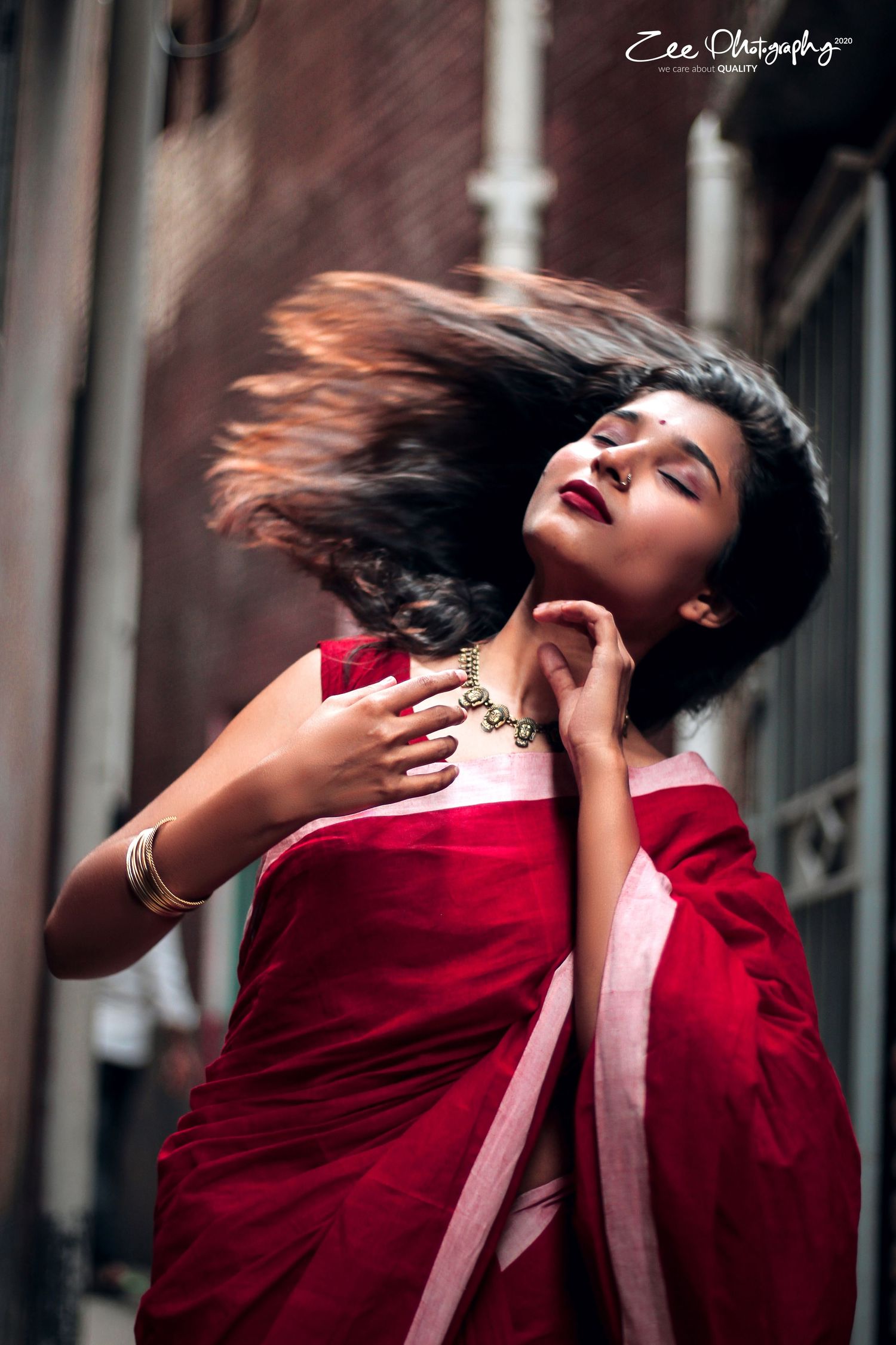 A dramatic portrait shows hair flowing while wearing a red and white sari.