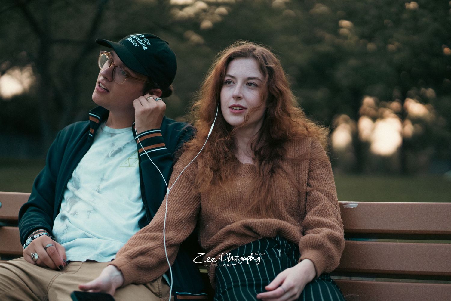 Two people sitting on a wooden bench in a park during sunset.