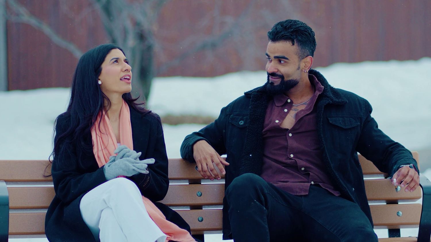 Two people laugh and chat while sitting together on a bench outdoors.