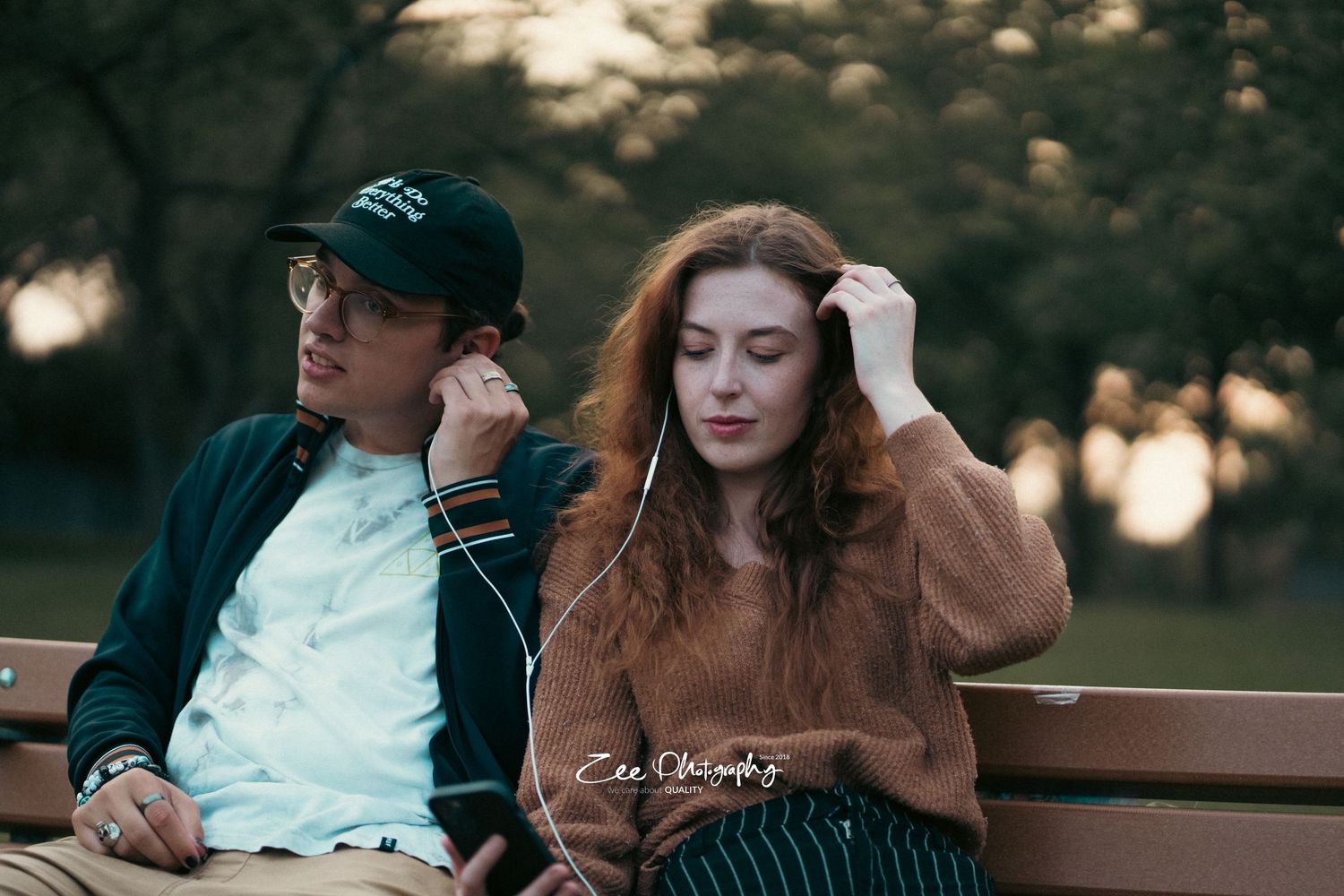 Couple sitting relaxed on park bench at dusk wearing casual autumn clothing.