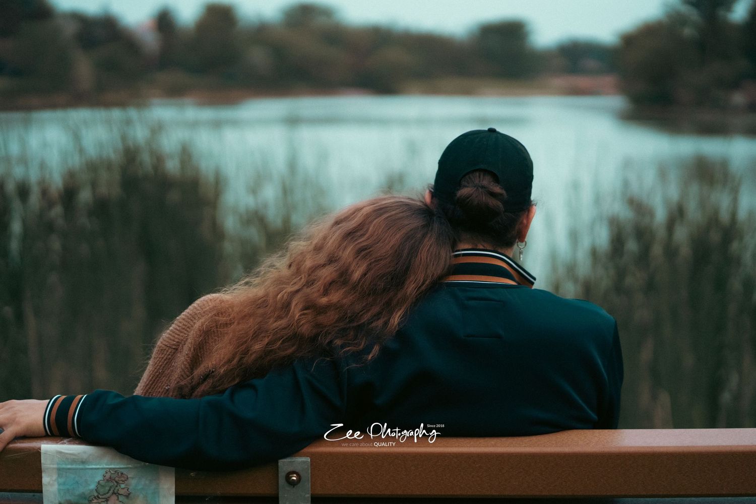 Couple sitting on bench overlooking serene lake view at sunset.