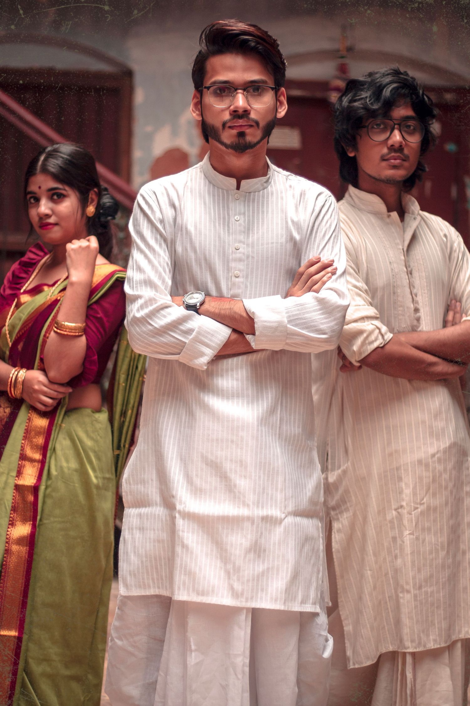 Three people in traditional South Asian attire pose together, wearing kurtas and traditional clothing.