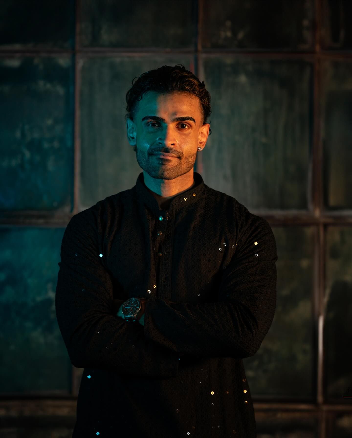 A person in a black jacket stands against a dark background with turquoise lighting creating a moody atmosphere.