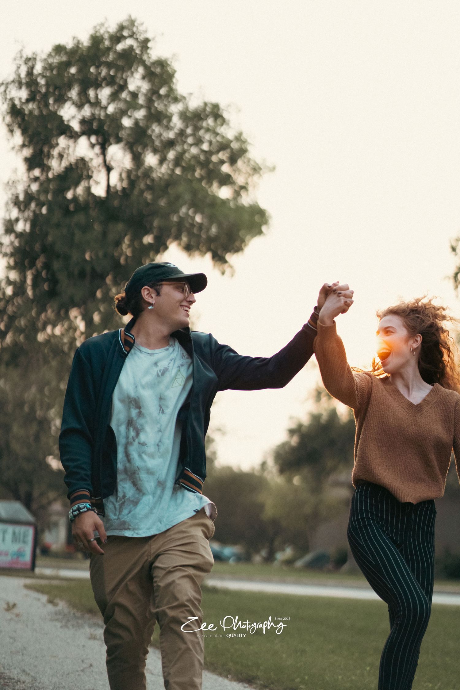 Couple holding hands up while dancing and laughing together in a park.