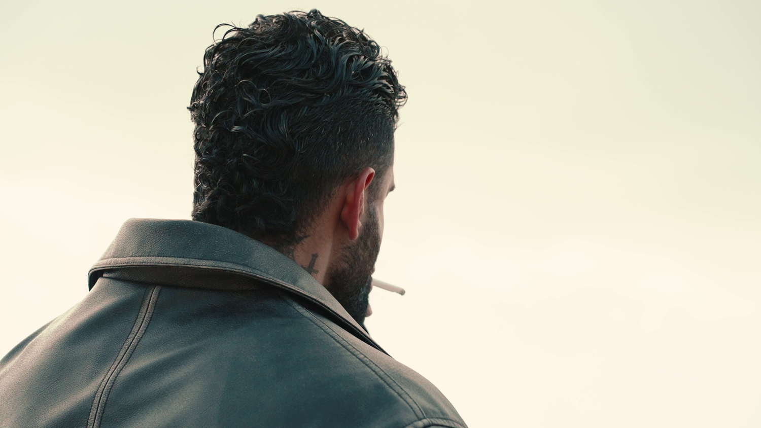 Back view of a person with dark hair wearing a jacket against a light background.
