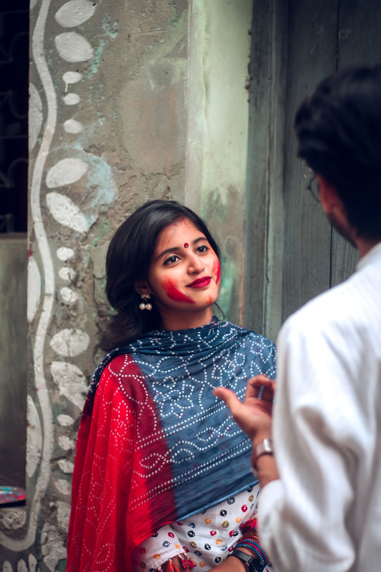 Colorful traditional sari worn with blue and red embroidered designs against a textured wall background.