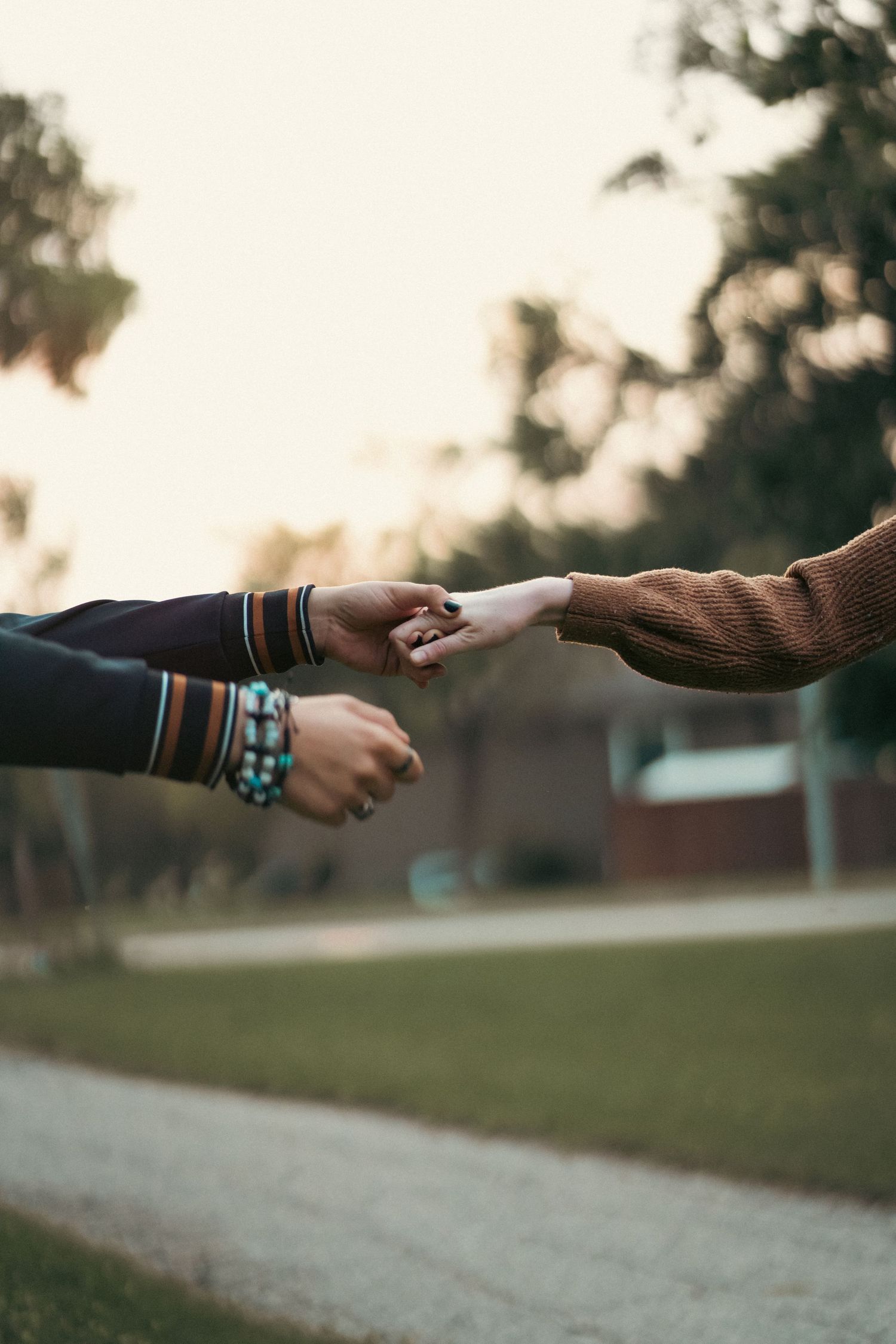 Close-up of hands reaching towards each other wearing bracelets during sunset.