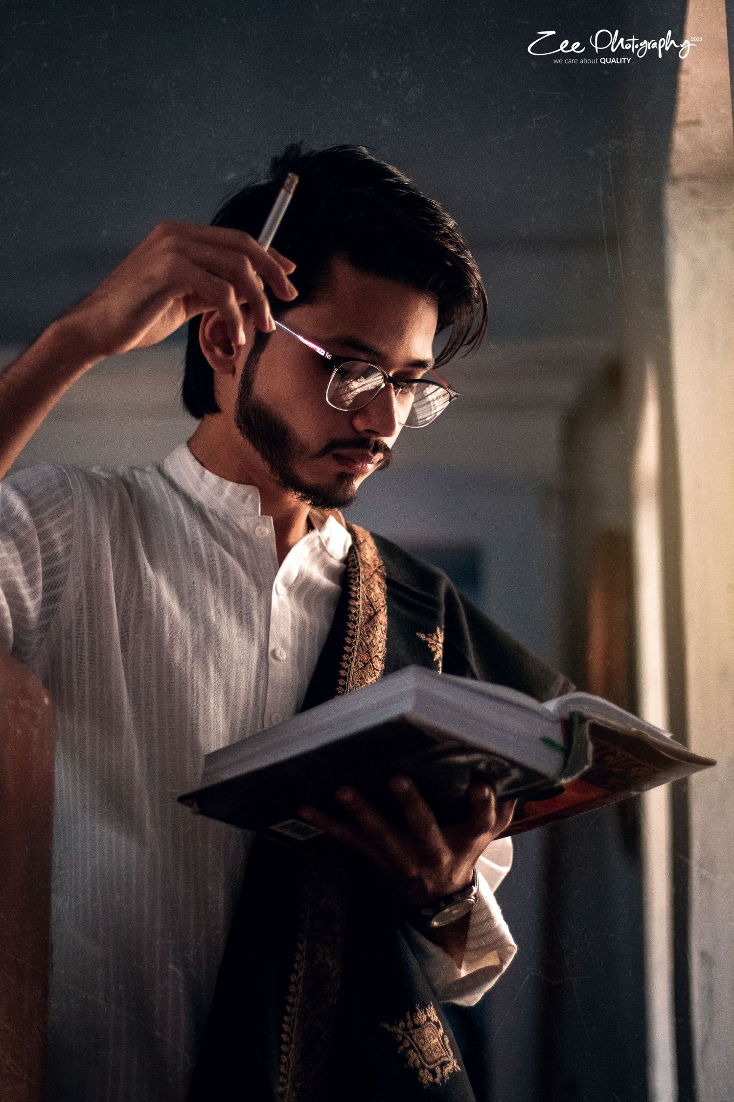 A person in glasses and traditional clothing studies intently while reading from a book in dramatic lighting.