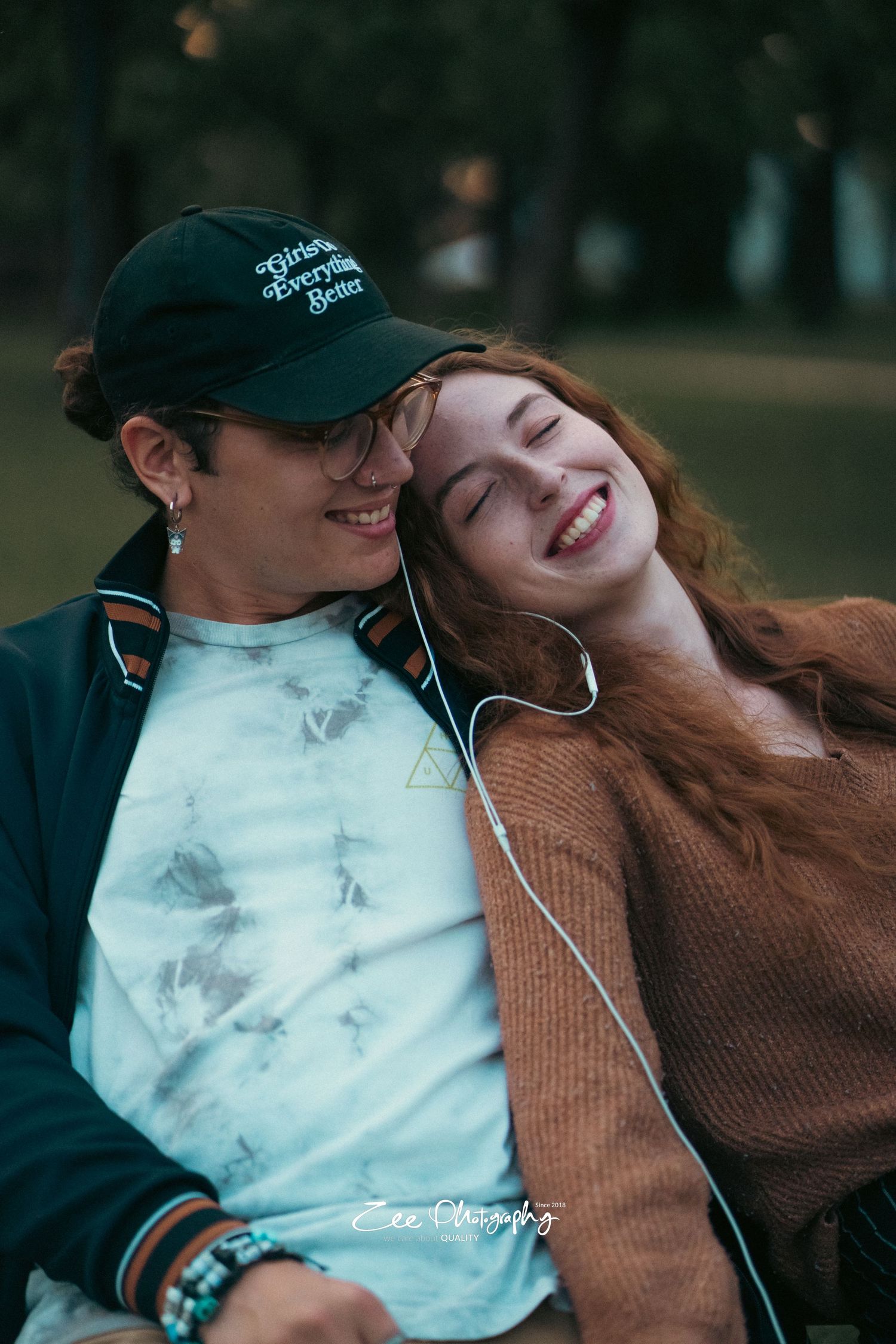 Couple sharing earbuds and smiling while sitting together on bench in park.
