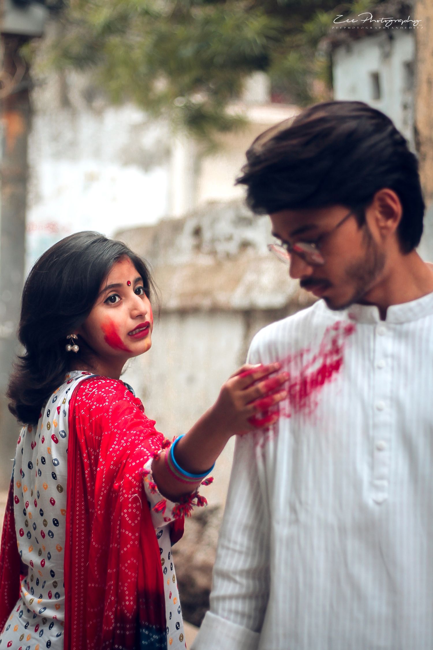 Couple celebrating Holi festival with red powder and traditional outfits.