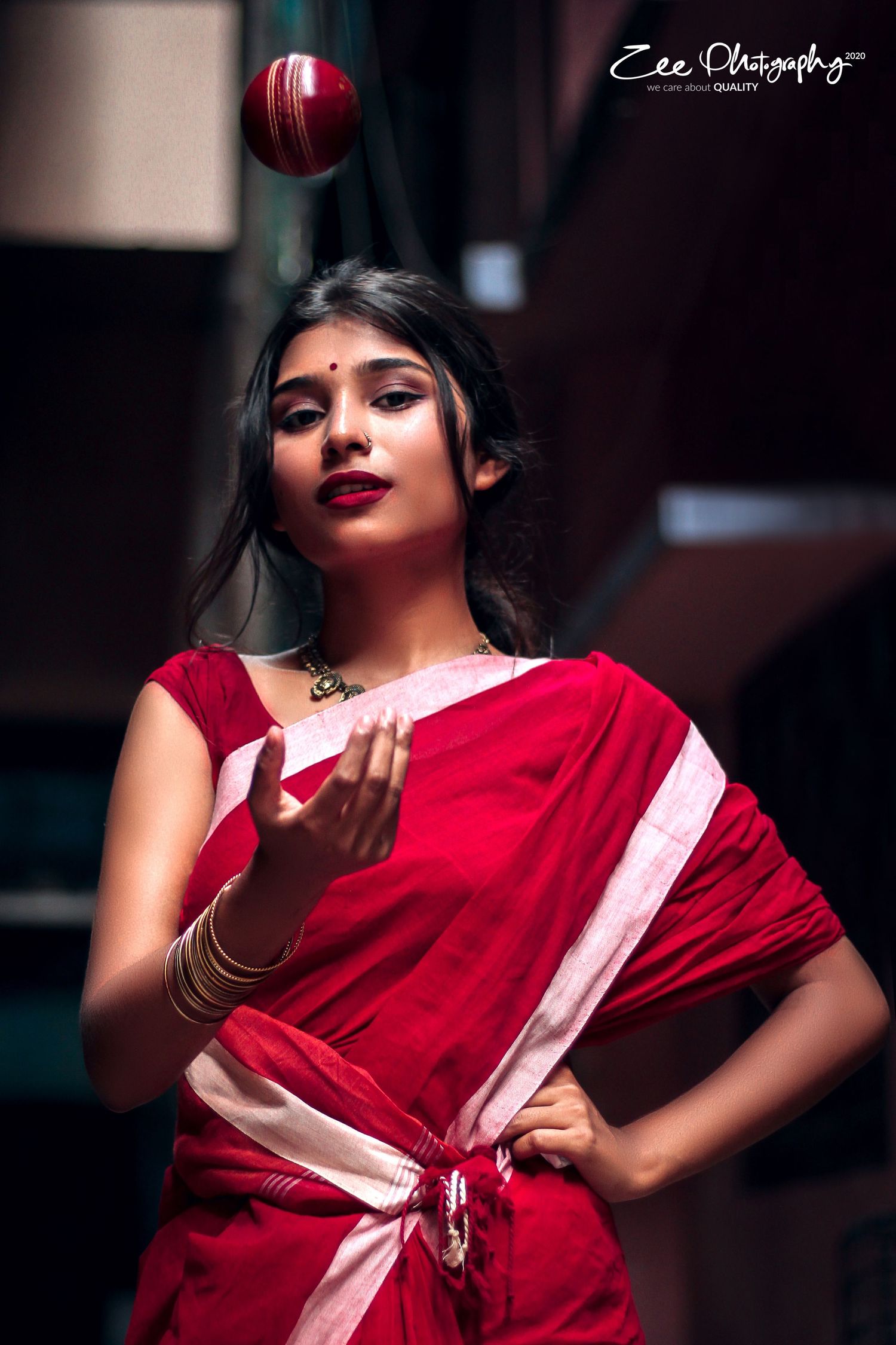 A festive photo with a cricket ball showing someone in red traditional attire making an elegant pose.