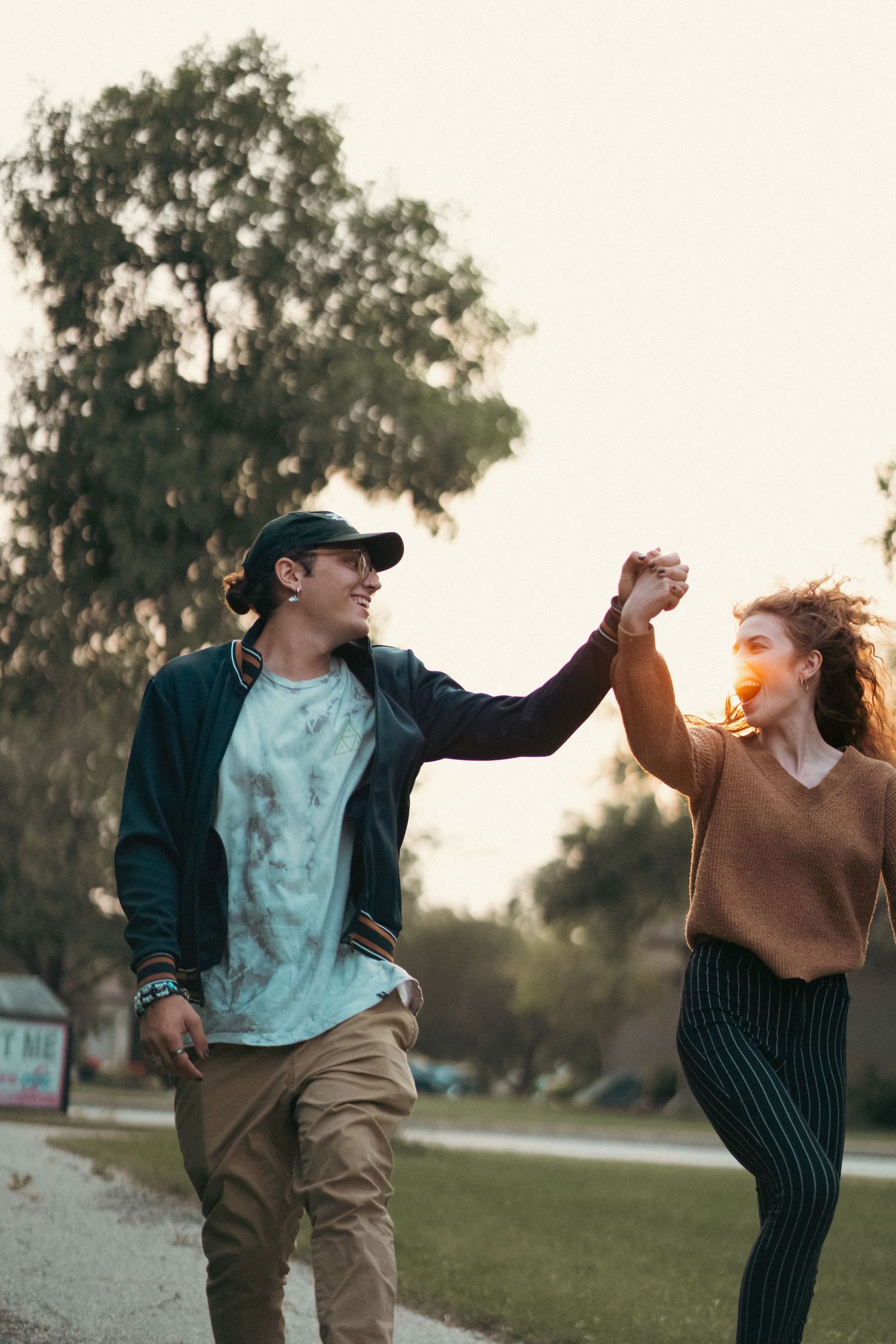 Two people dancing and holding hands in a park at sunset while enjoying a carefree moment together.