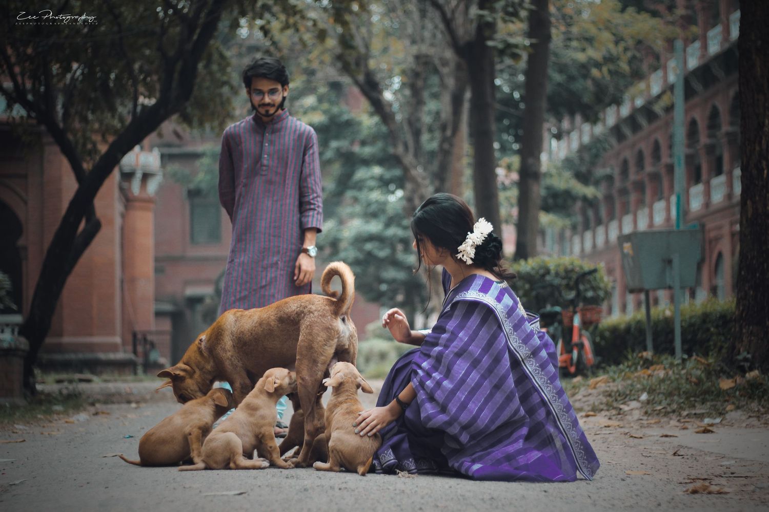 A couple in purple attire poses with dogs in a peaceful urban park setting.