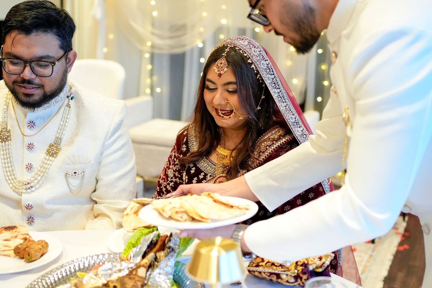 Guests enjoying a traditional Indian wedding feast while seated at elegant white tables with gold accents.