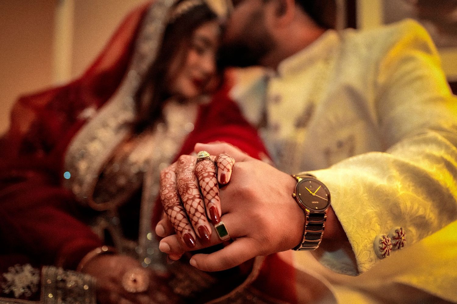 Hands with traditional henna designs and a gold watch during a South Asian wedding ceremony.