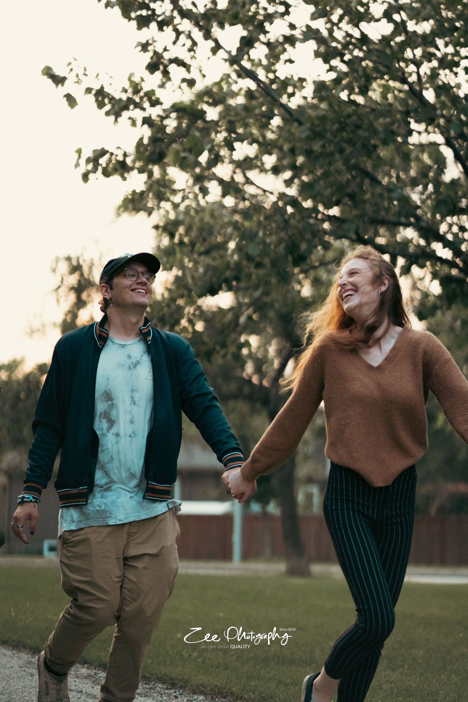 Couple holding hands while walking and laughing together on a park path.